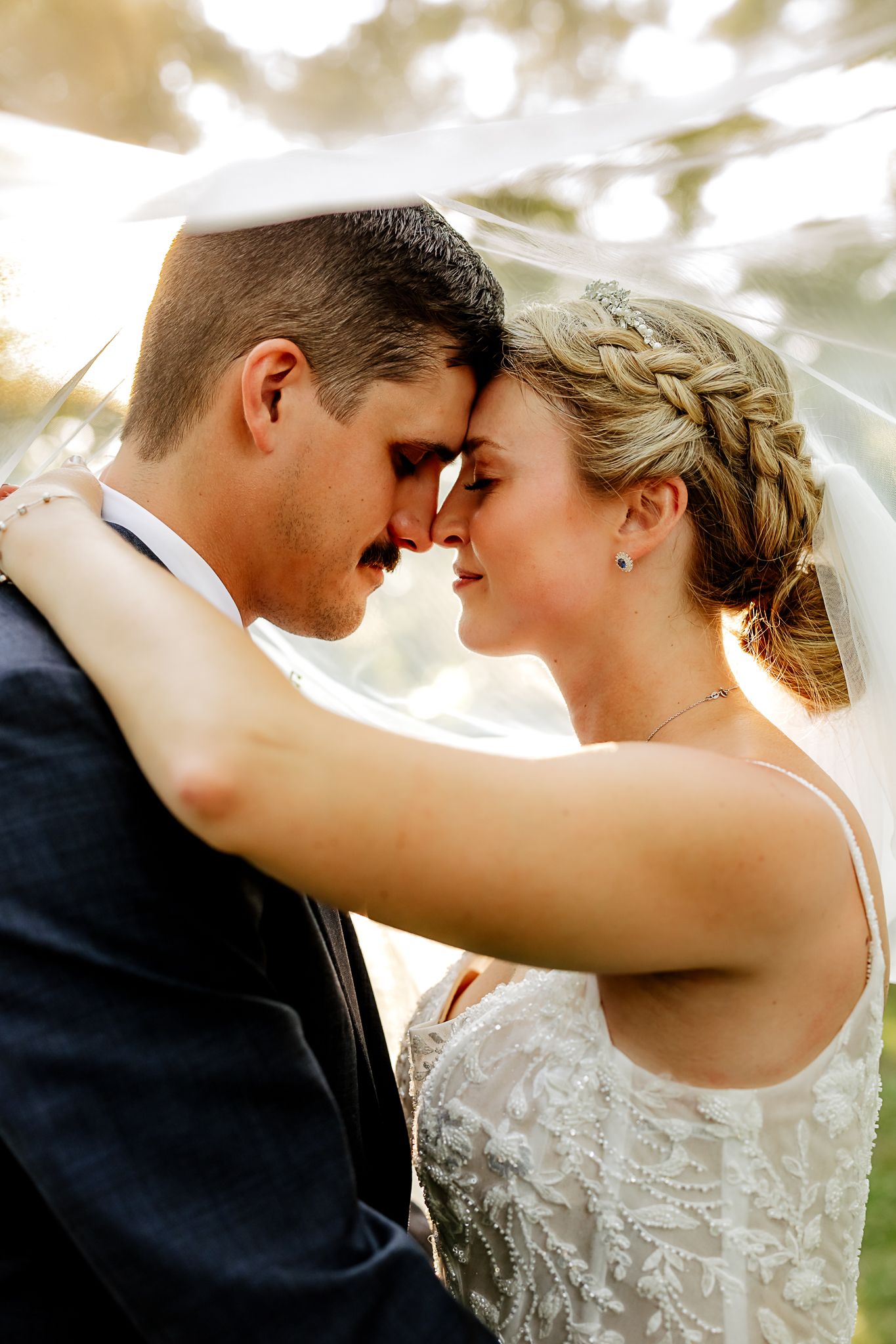 A bride and groom touch foreheads tenderly under a veil on their wedding day.