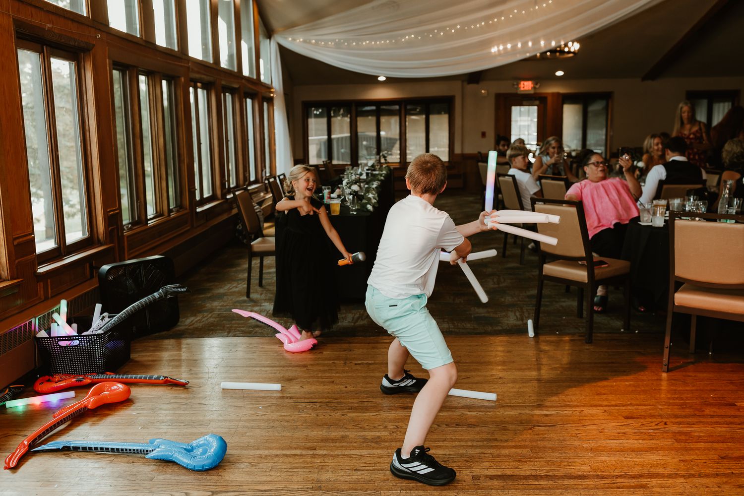 Children playing with toy guitars and light sabers on a dance floor at a wedding reception venue.