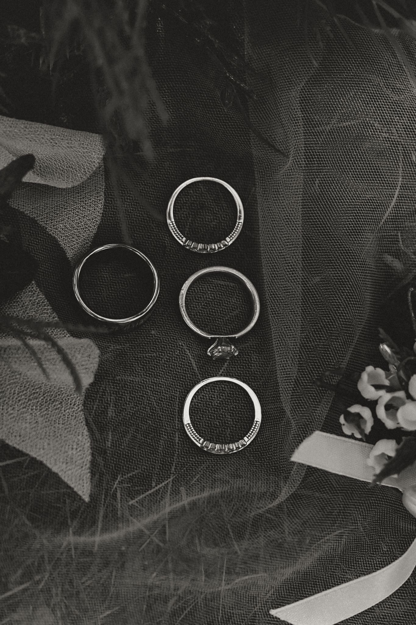 Black and white photo of three silver wedding rings displayed on dark mesh fabric.