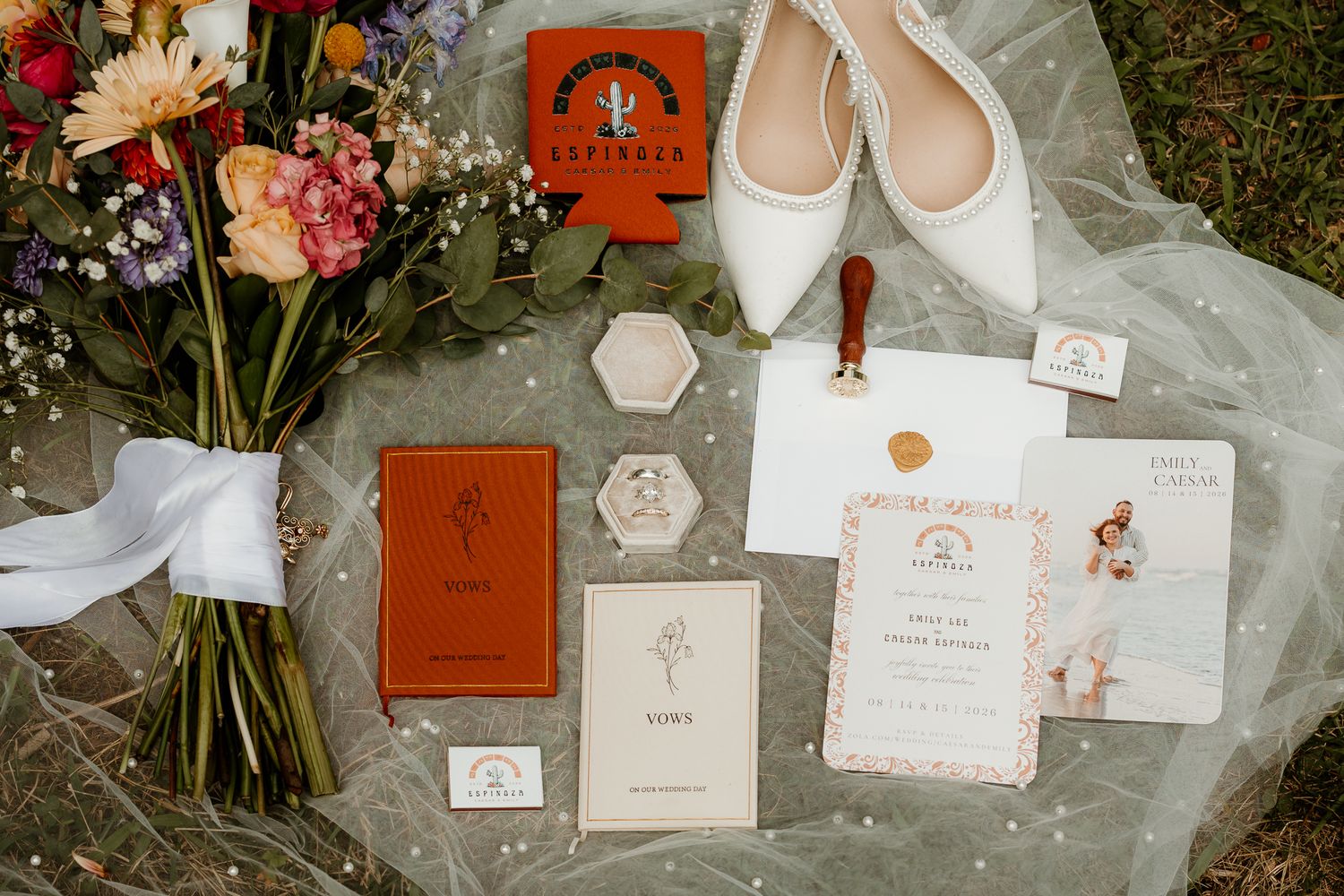 Wedding flat lay featuring floral bouquet, white heels, invitations, vow books, and terracotta stationery suite on sheer fabric.