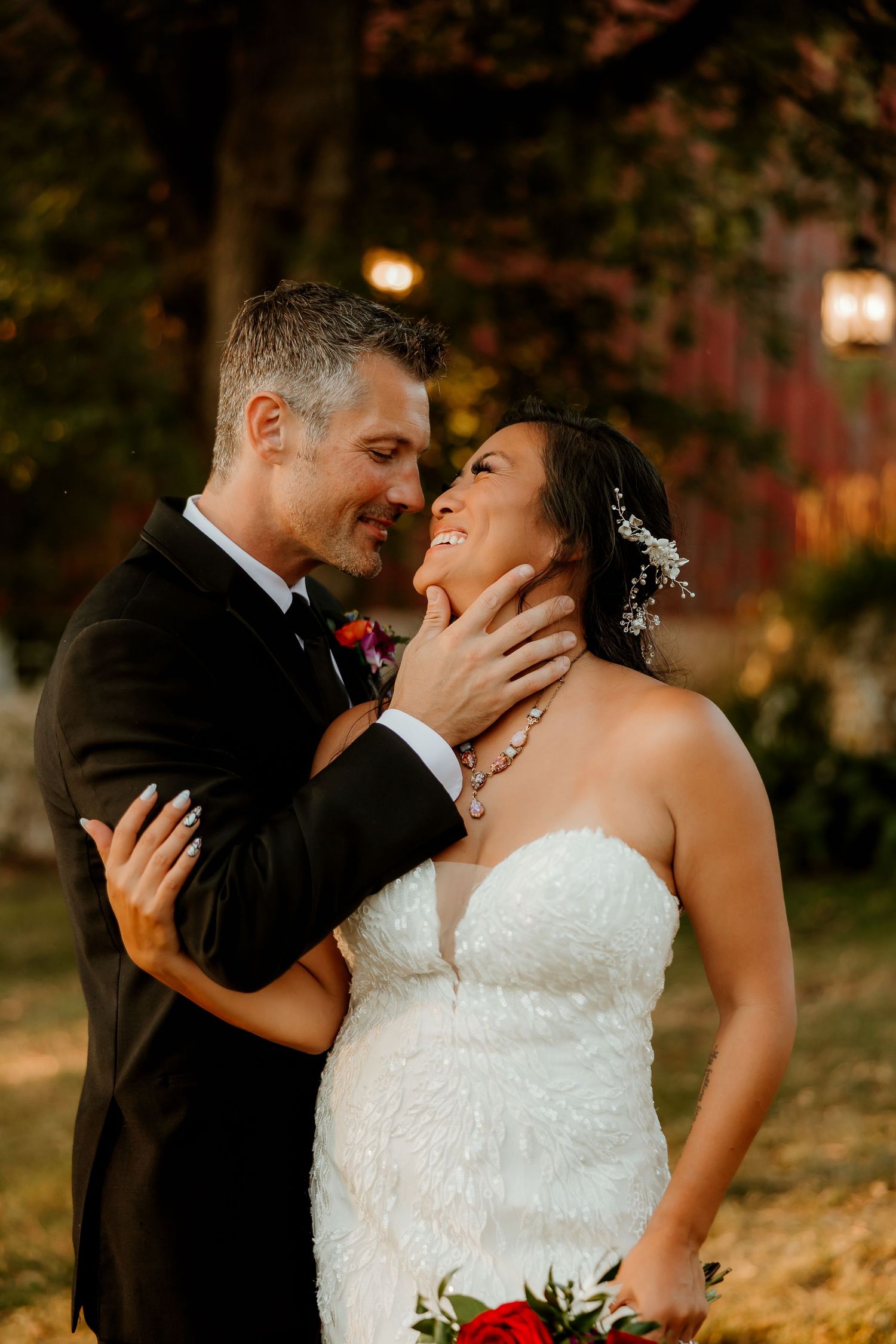 A groom tenderly holds his bride's face as she smiles up at him outdoors during a romantic evening wedding portrait.
