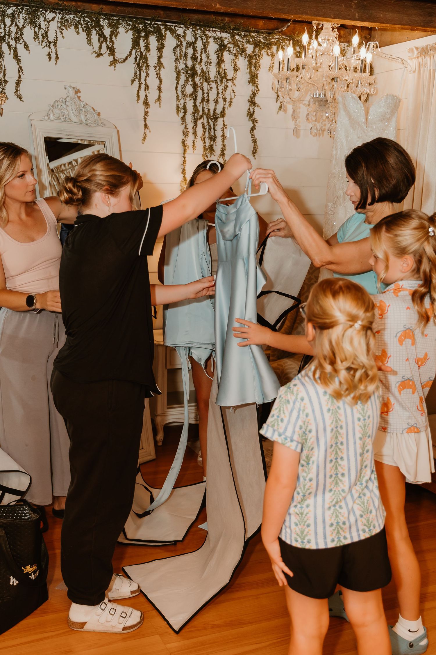 Women gathering around a light blue bridesmaid dress on a hanger in an elegant bridal suite with chandelier.