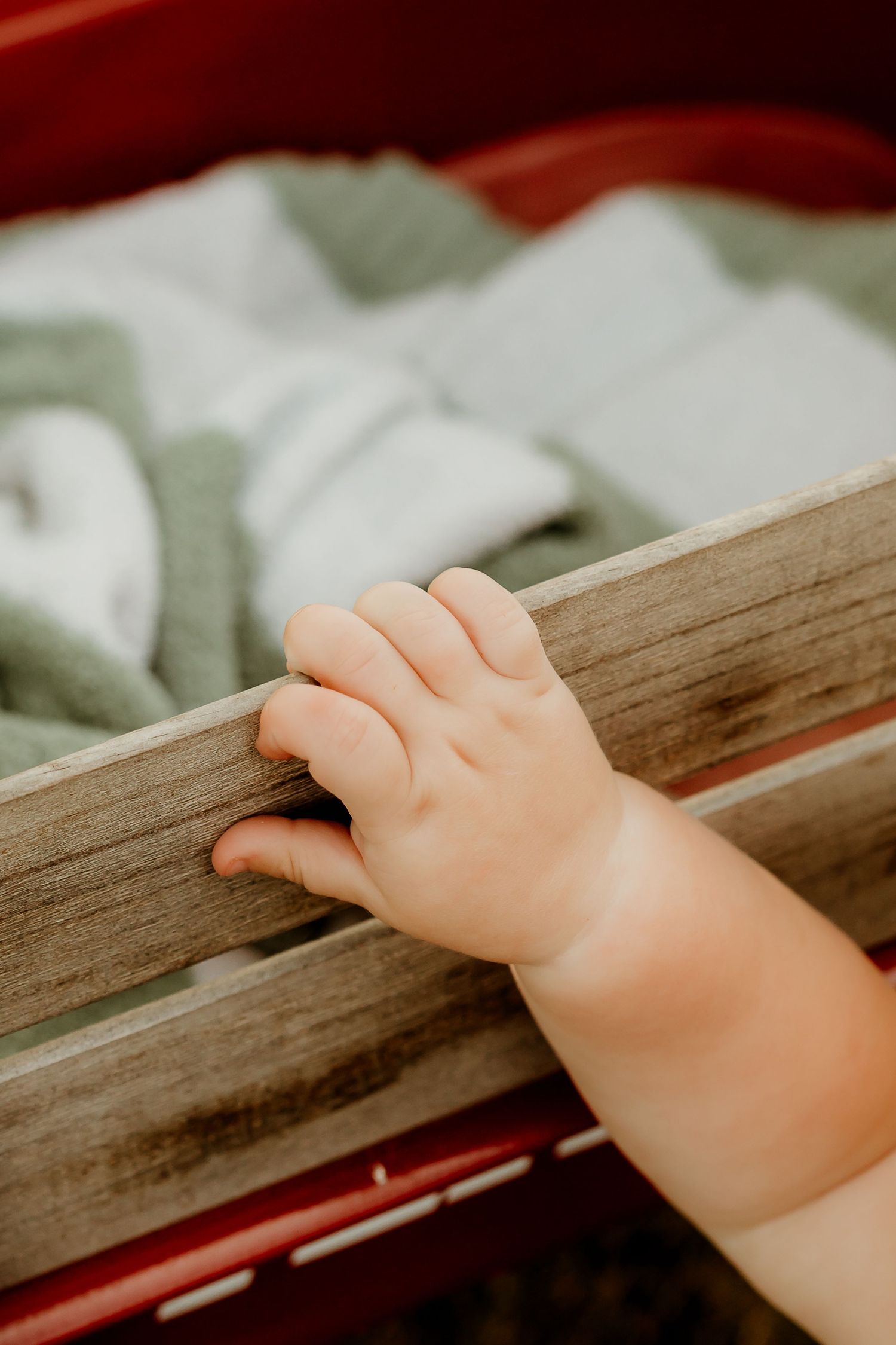 Close-up of a baby's hand gripping the wooden rail of a crib with green blankets inside.