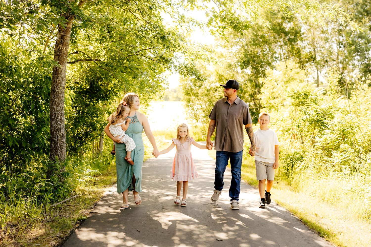 Family of five walking hand-in-hand down a sunny tree-lined path.