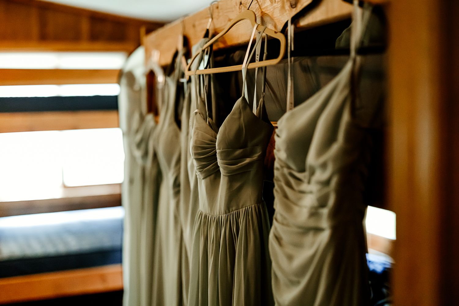 Sage green bridesmaid dresses hanging on wooden hangers in a rustic cabin room before a wedding ceremony.