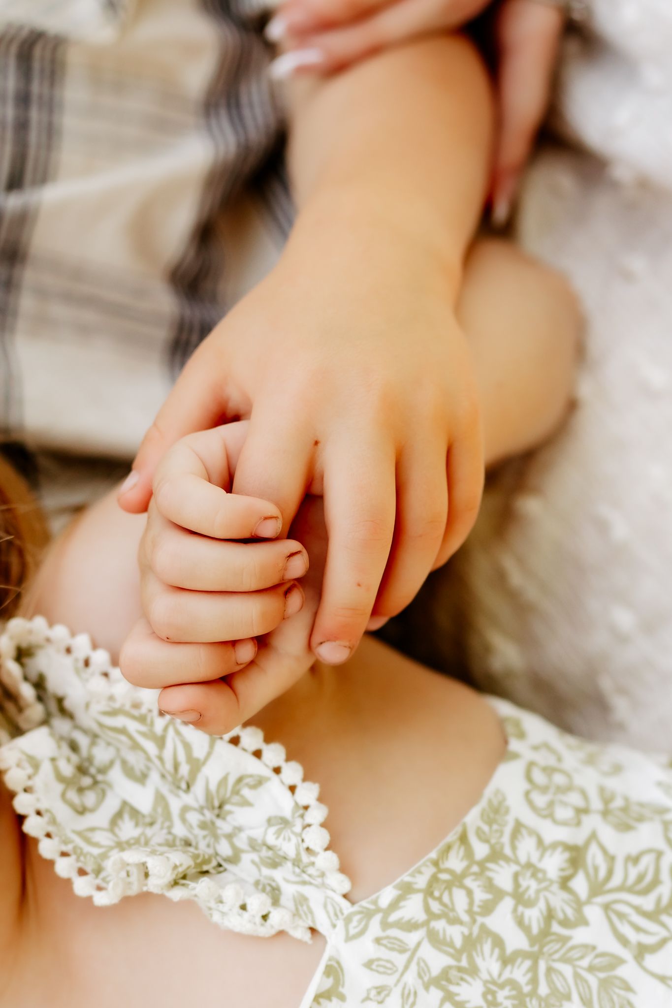 A close-up of two young children holding hands tenderly during an outdoor family photo session.