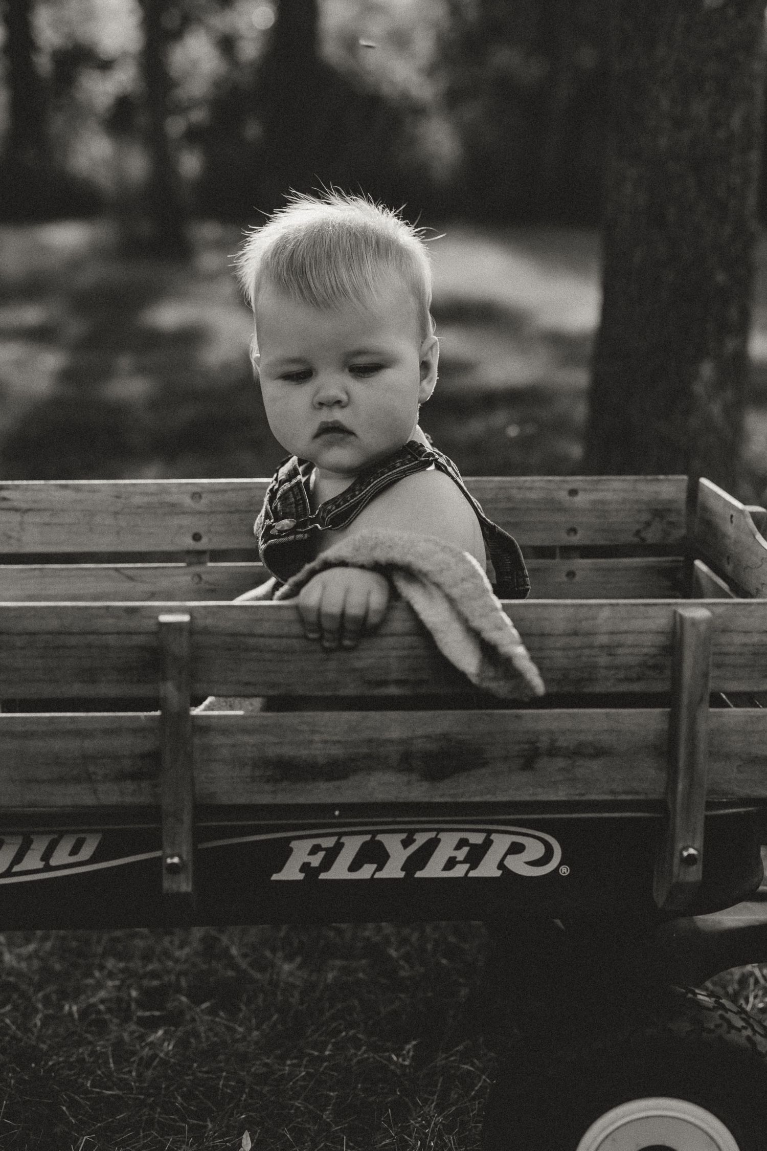 Black and white photo of a toddler sitting in a Radio Flyer wooden wagon outdoors.