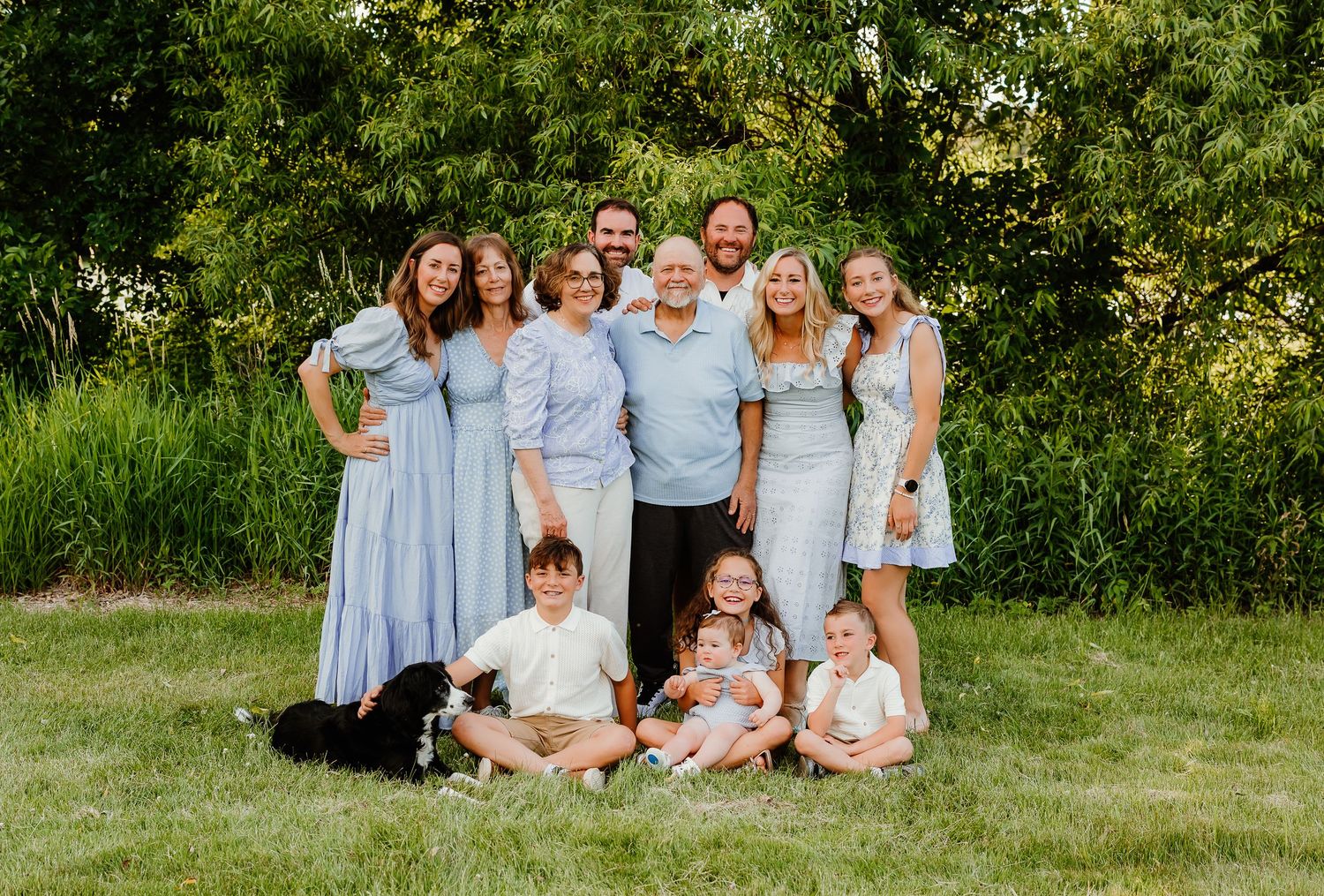 Large extended family posing together on green lawn in coordinating blue outfits with children and dog in front.
