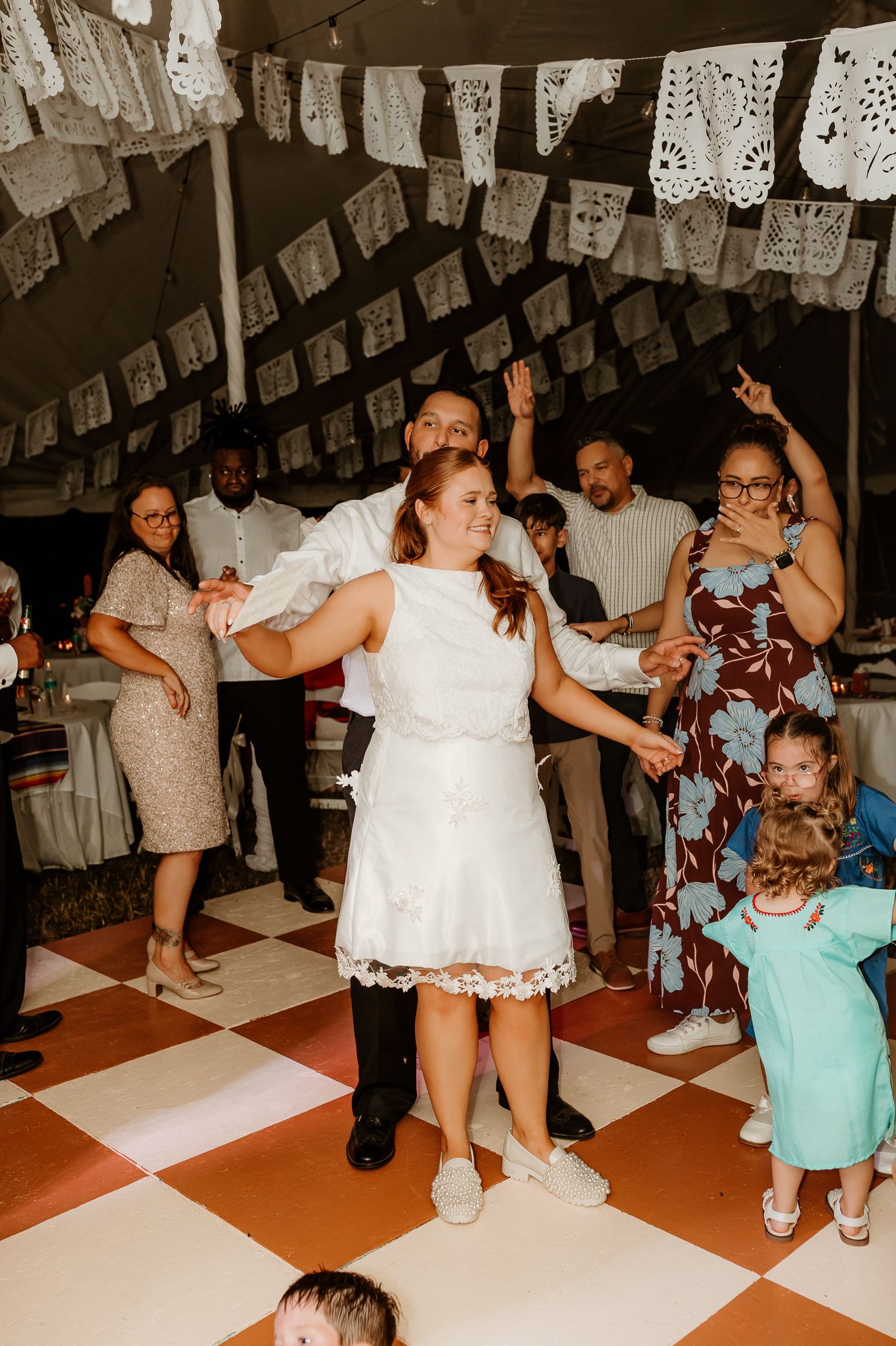 Bride and groom dancing joyfully at wedding reception under decorative paper bunting on checkered dance floor.