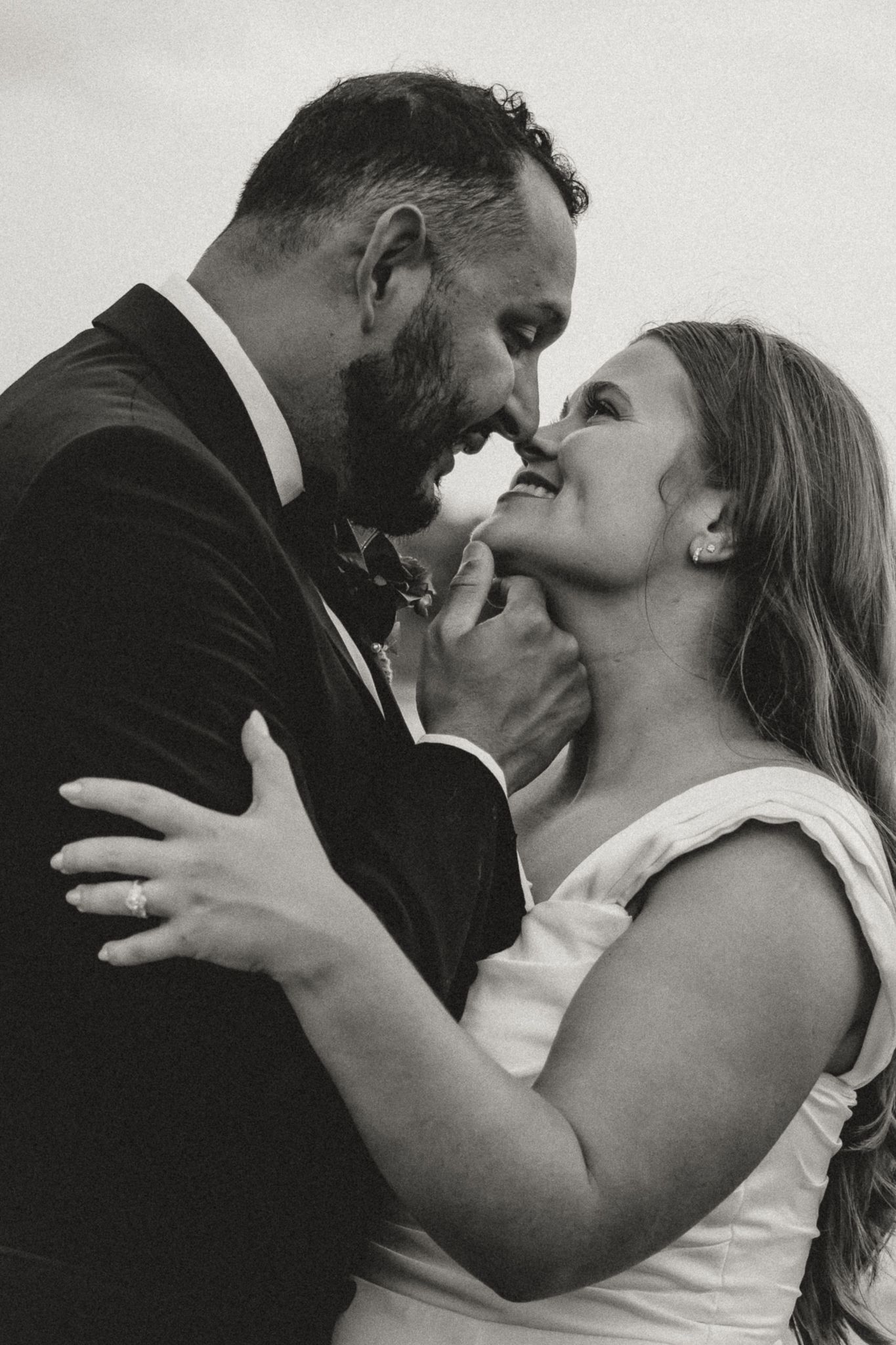 Black and white wedding photo of bride and groom sharing an intimate moment, nearly kissing, dressed in formal attire.