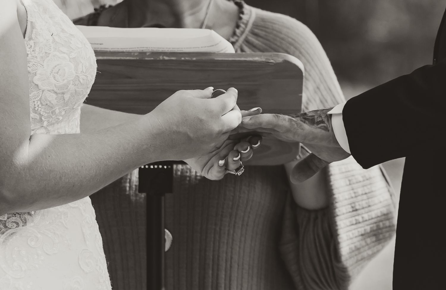 Black and white wedding photo of bride and groom exchanging rings at the altar.