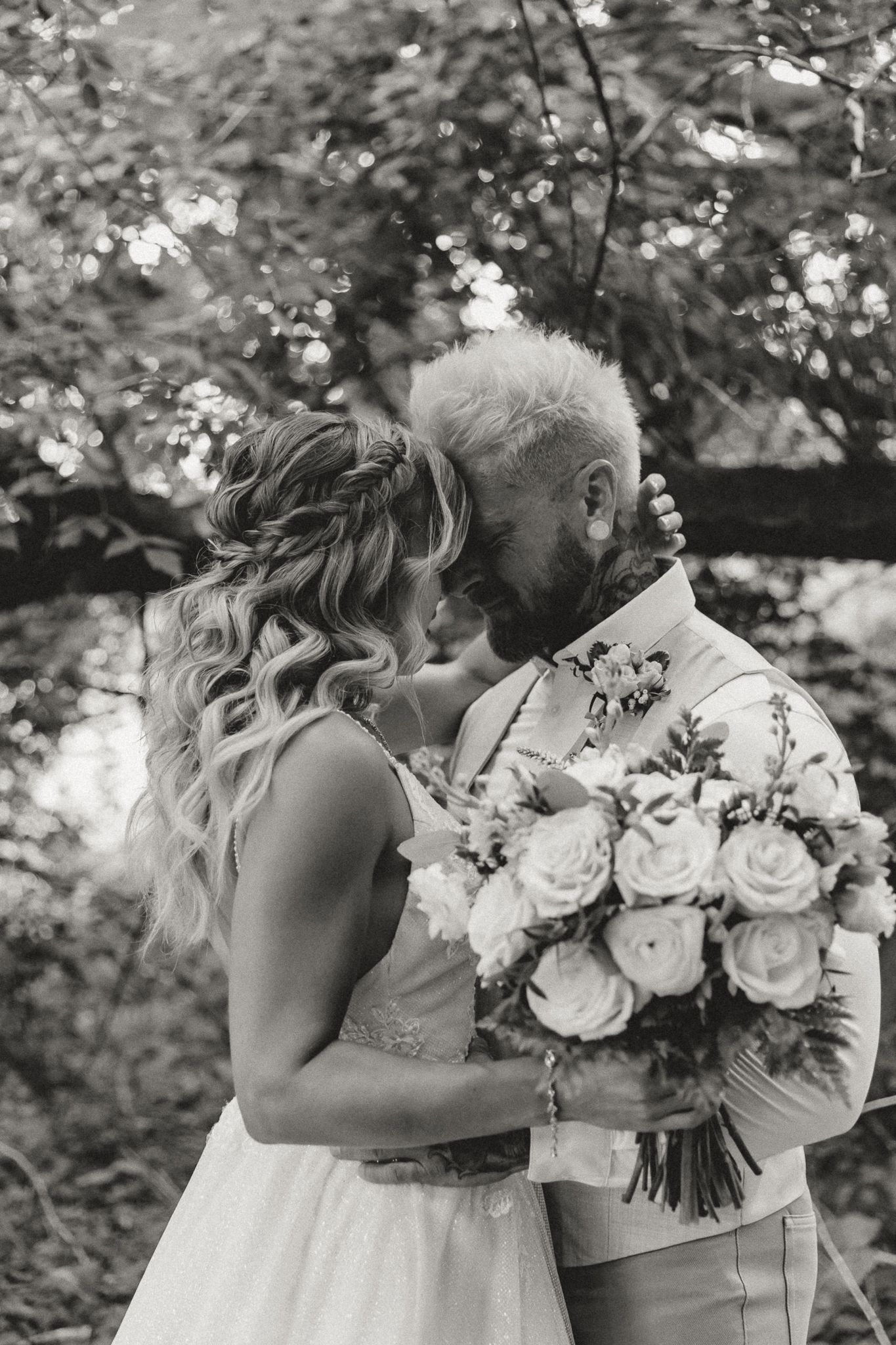 Black and white wedding photo of bride and groom sharing a romantic moment, bride holding a bouquet of roses outdoors.