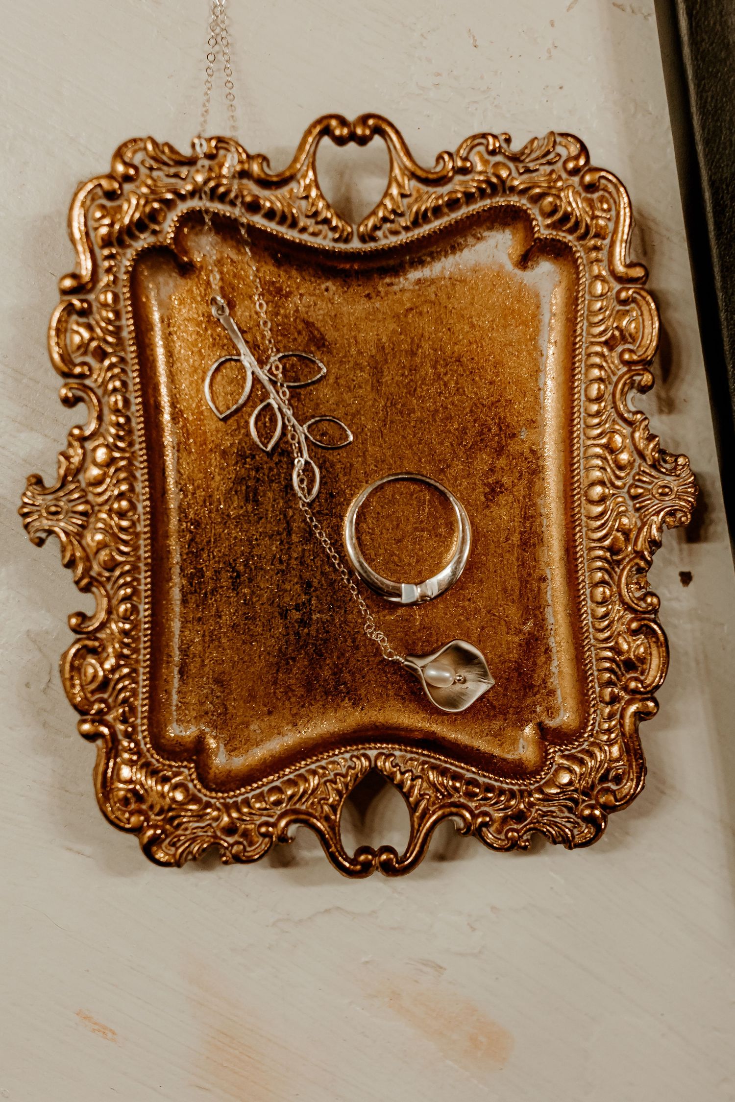 Silver leaf pendant necklace and a silver ring resting on an ornate antique gold tray with brown velvet lining.