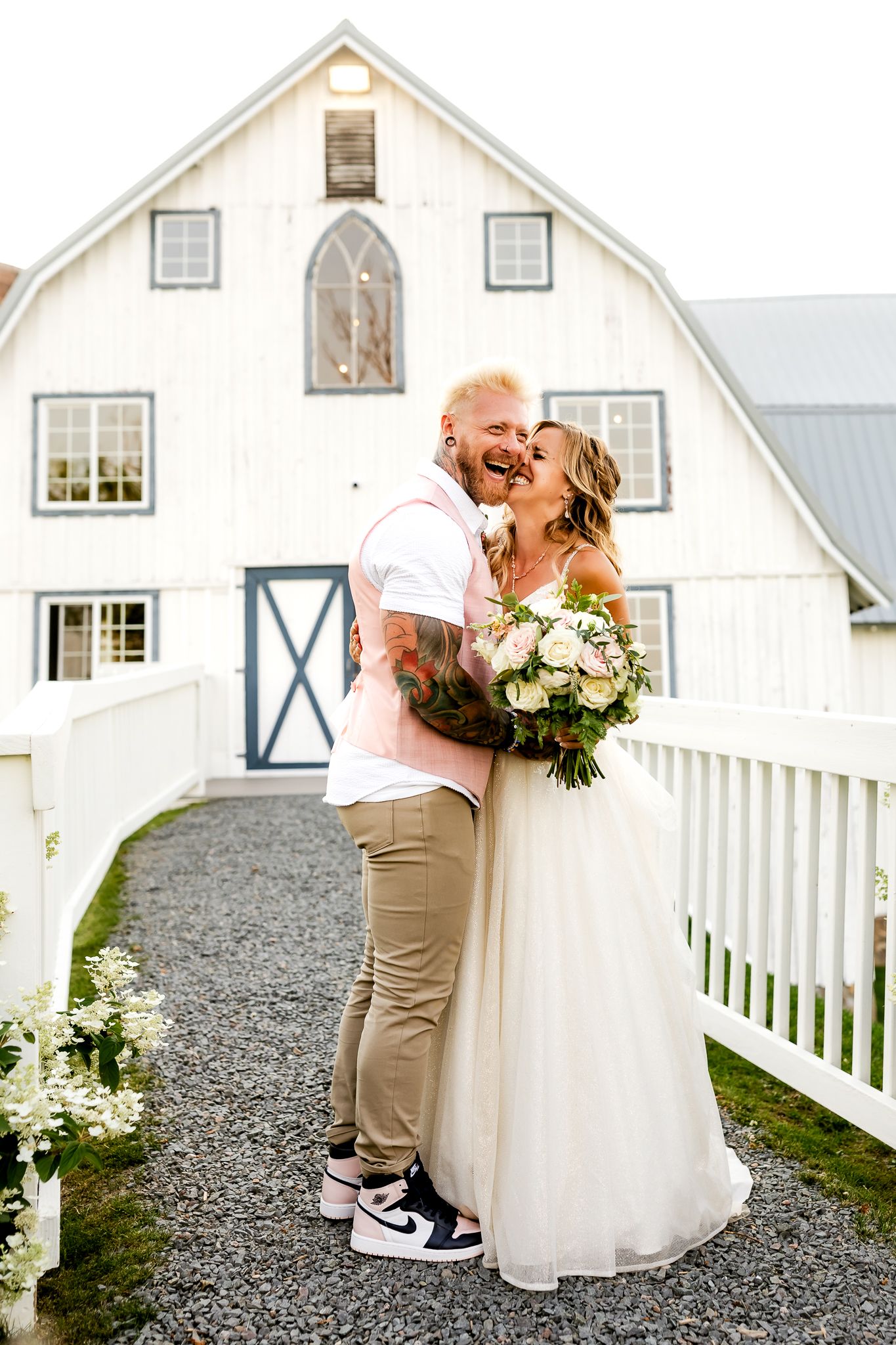 Bride and groom sharing a romantic kiss outside a white barn venue, bride holding a white floral bouquet.