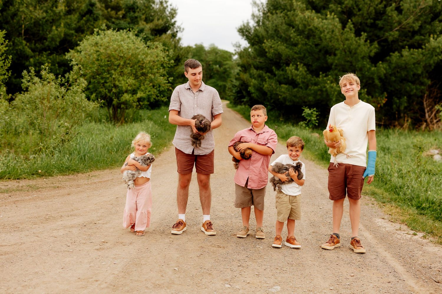 Five children holding puppies while standing together on a country dirt road.