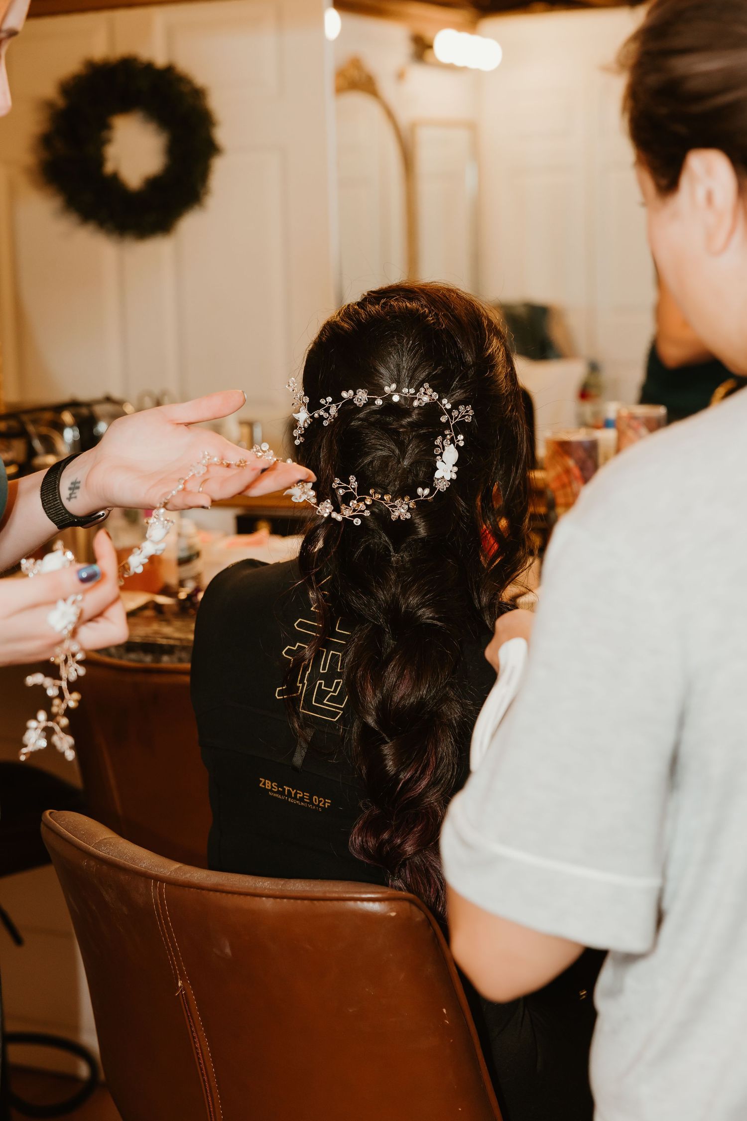 Bride getting floral hair accessories placed in elegant braided updo by hairstylist in bridal salon.