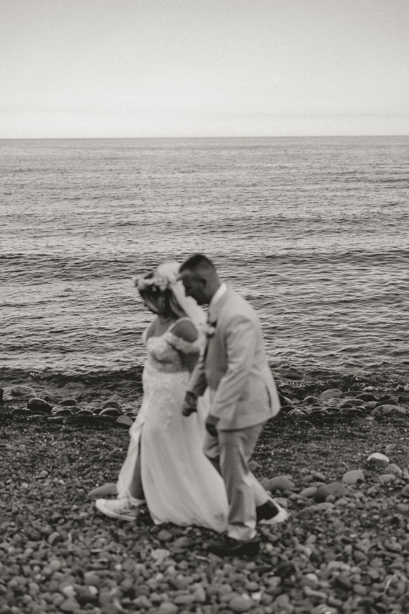 Black and white photo of a bride and groom sharing a romantic moment on a rocky beach by the ocean.