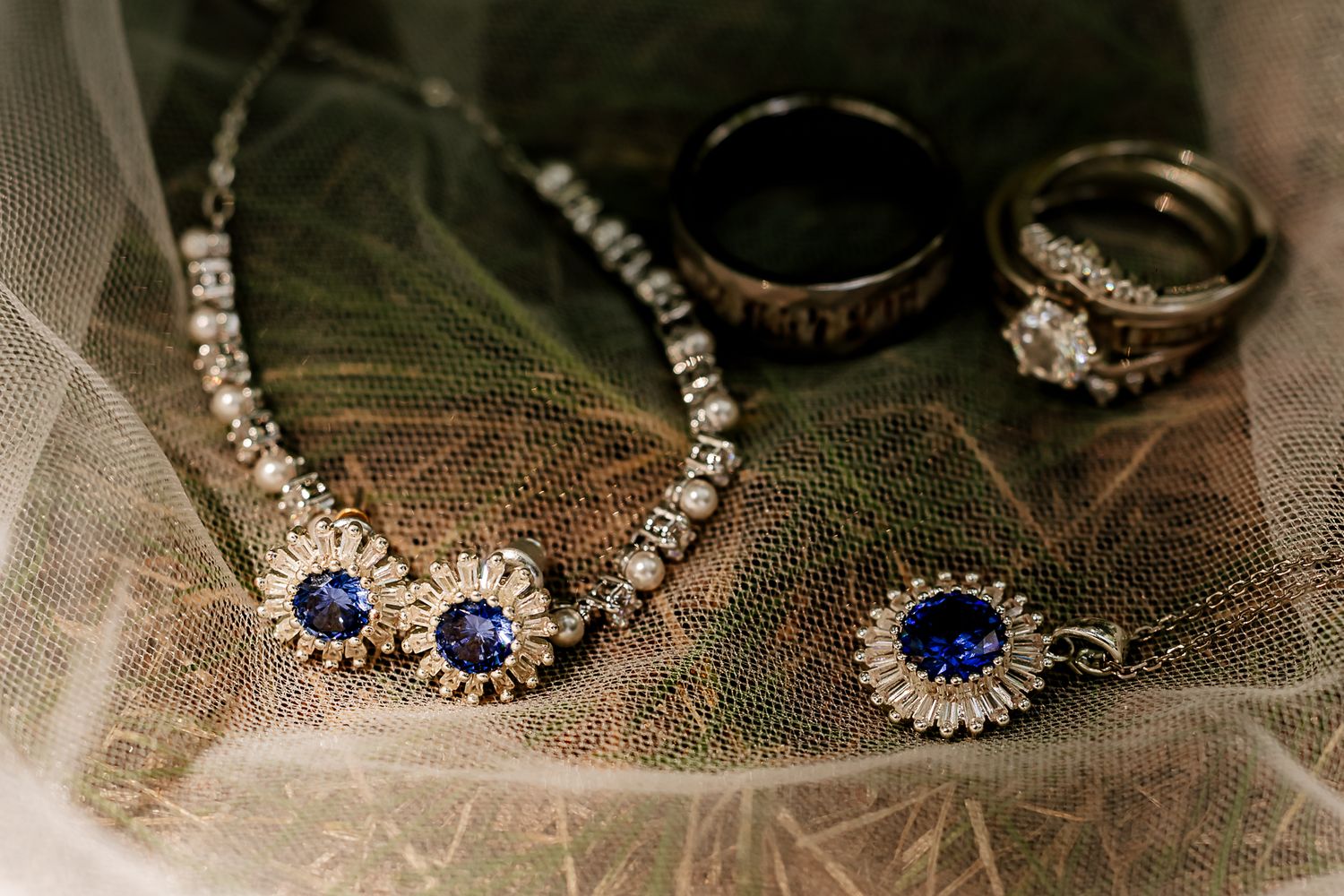 Elegant bridal jewelry set featuring sapphire and diamond necklace, matching earrings, and rings on a leaf background.