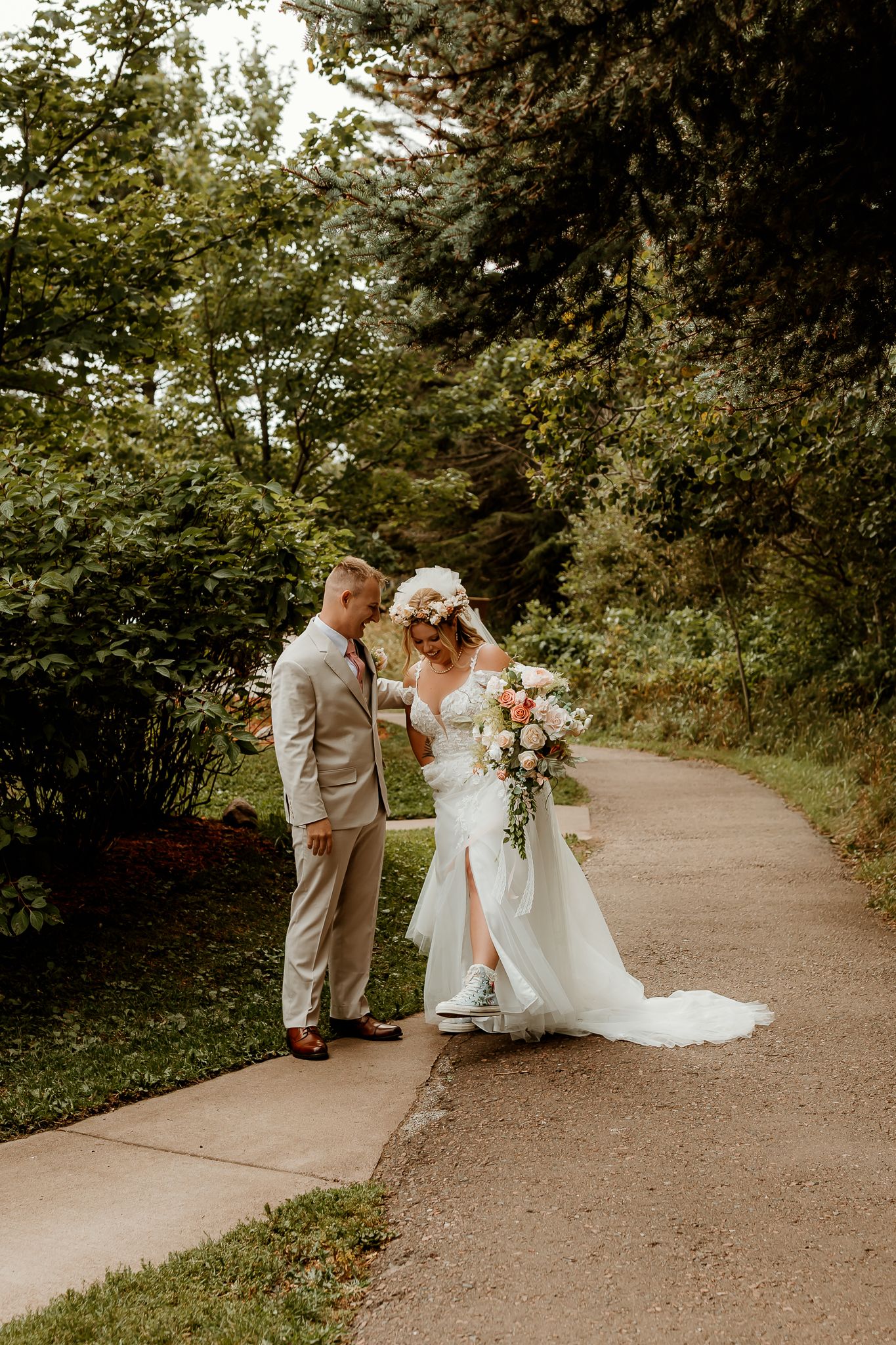 Bride and groom walking on a garden path, bride holding a pink bouquet and wearing a floral crown on their wedding day.