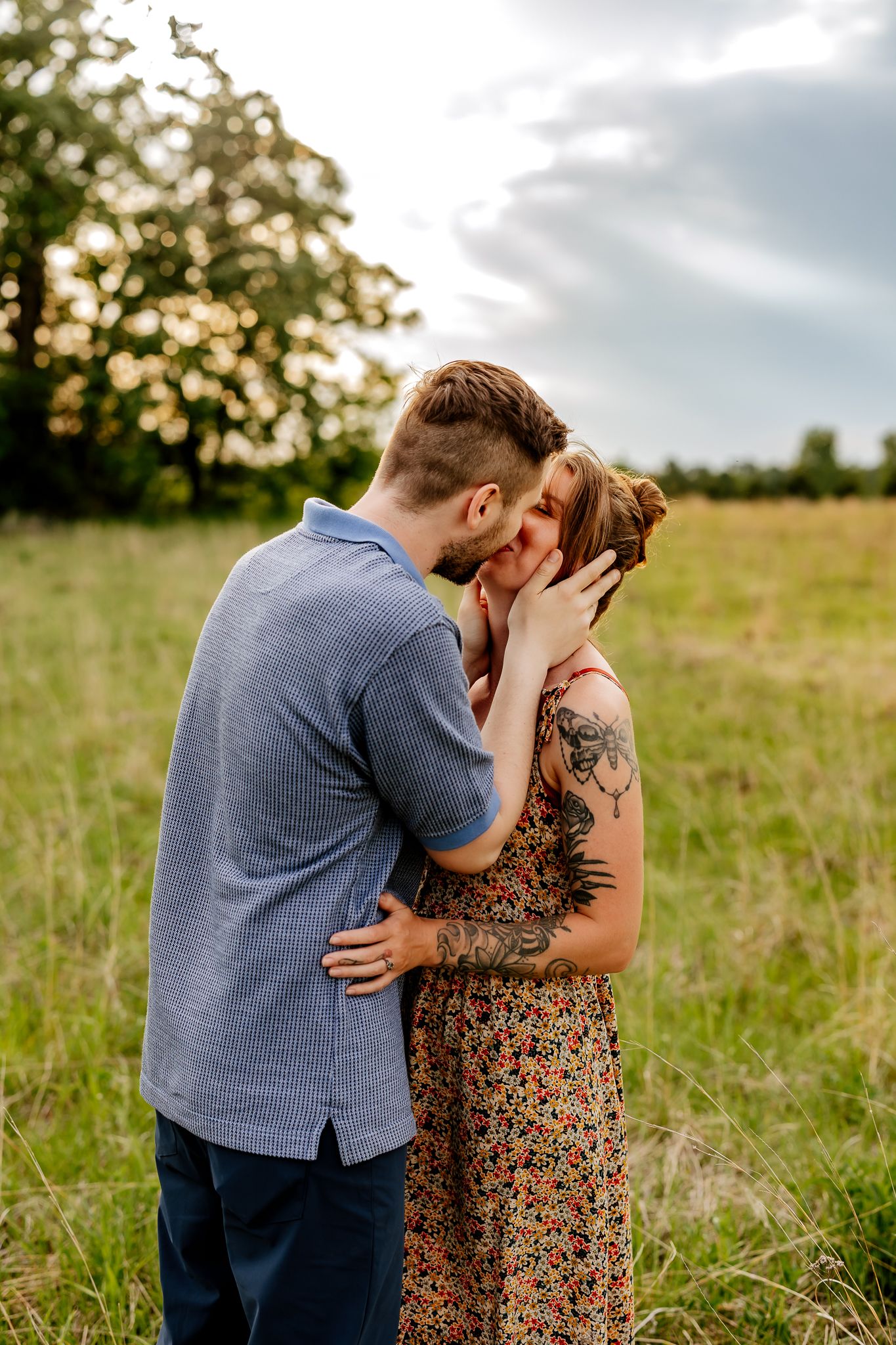 A couple shares an intimate moment in a green meadow, the man gently cradling the tattooed woman's face.