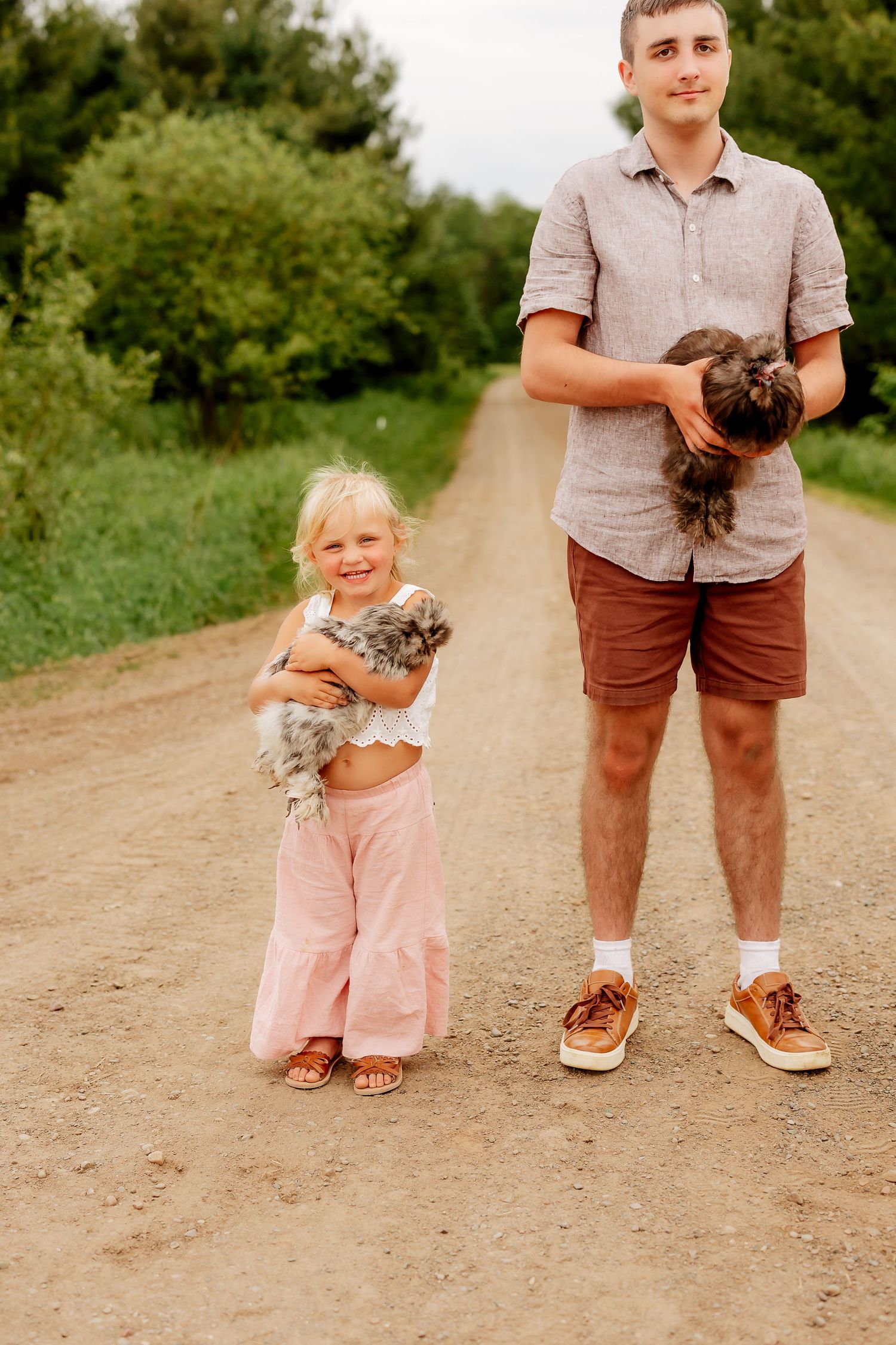 Young man and little girl holding fluffy kittens on a rural dirt road.