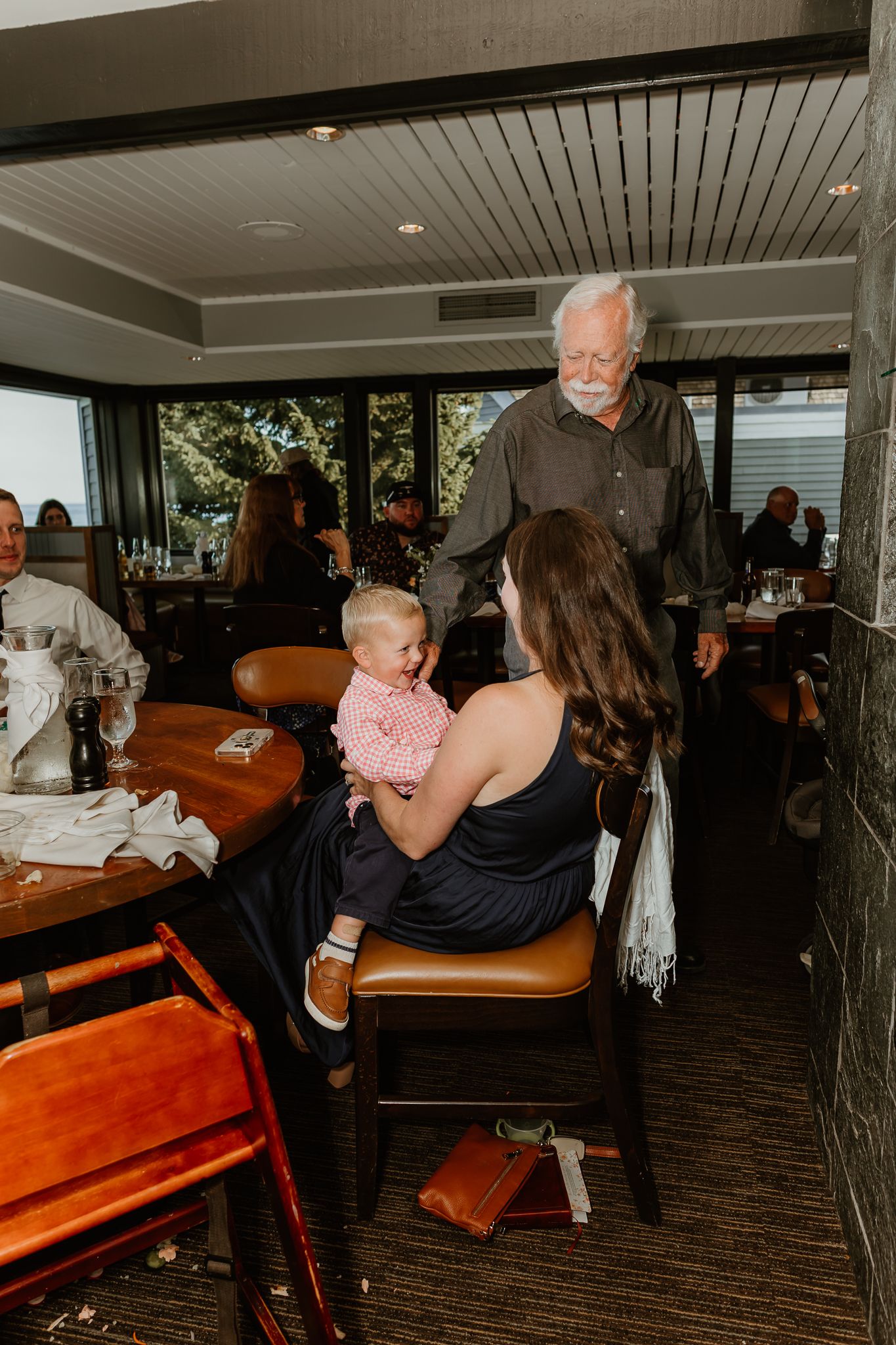 Family gathering at a restaurant with a woman holding a baby and an elderly man standing nearby.
