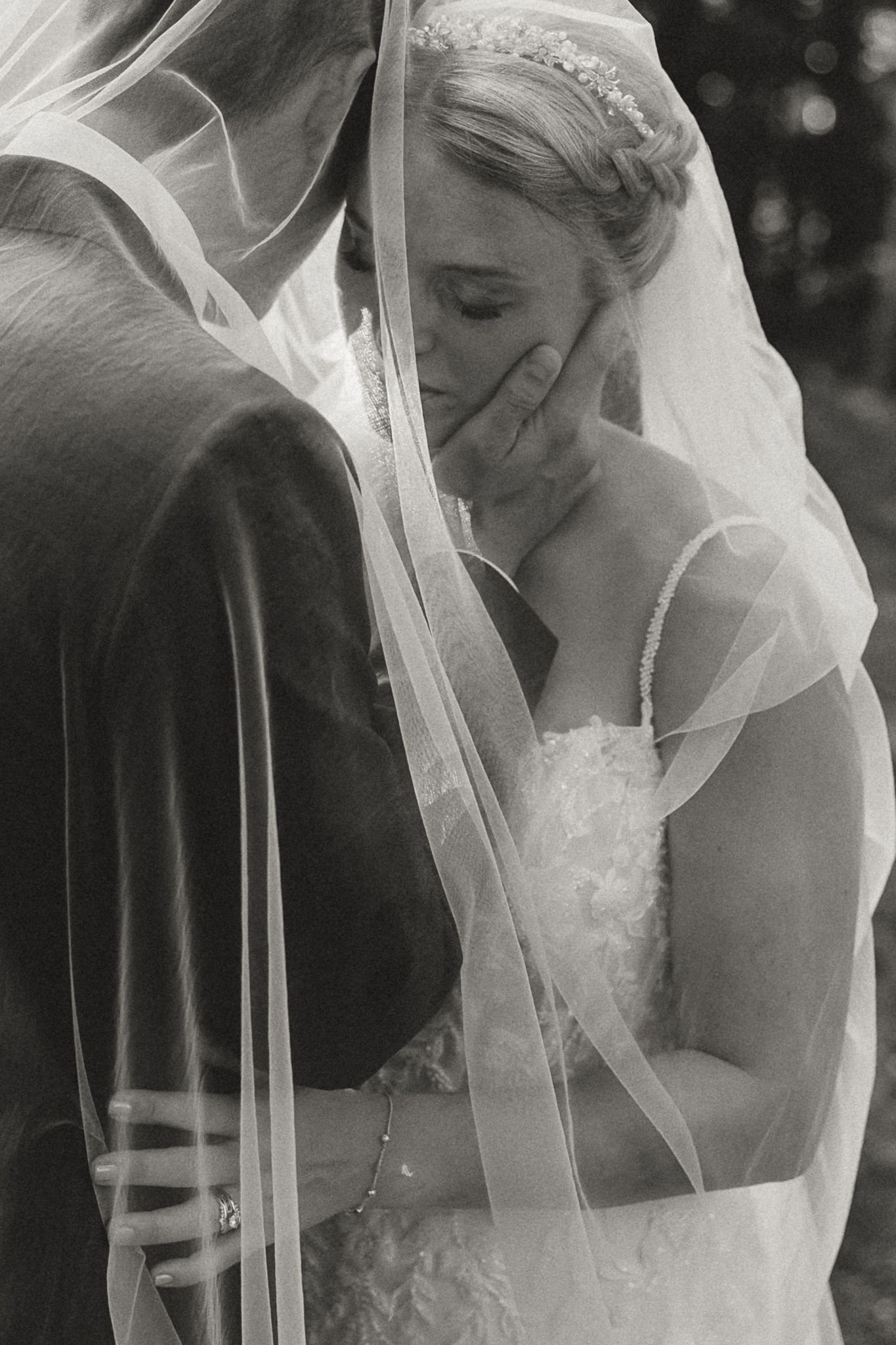 Black and white wedding photo of bride in veil and gown embracing groom, touching her face emotionally.