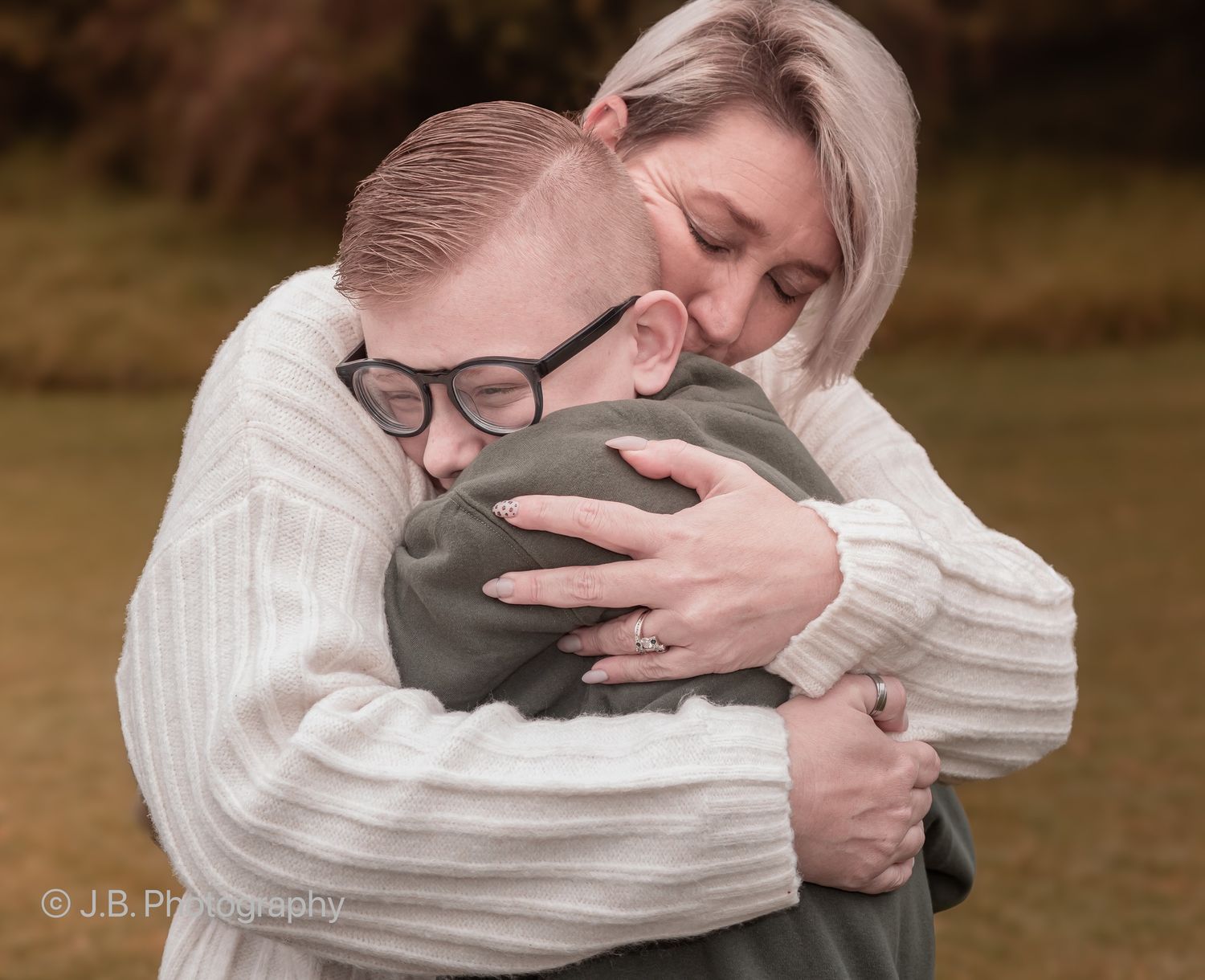 Blonde woman in white sweater sharing a tender hug with a young boy outdoors.