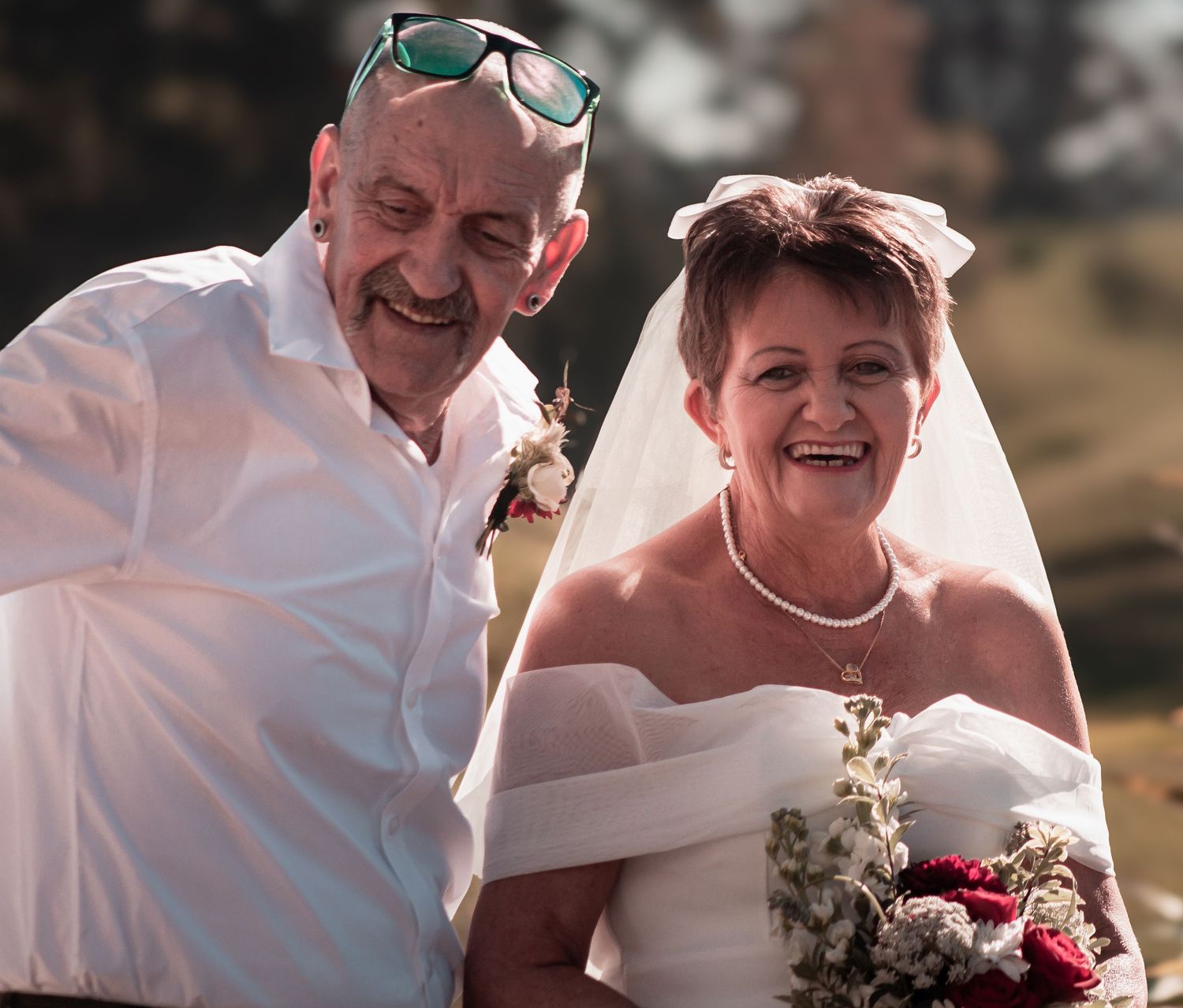 Joyful mature bride and groom laughing together outdoors on sunny wedding day.