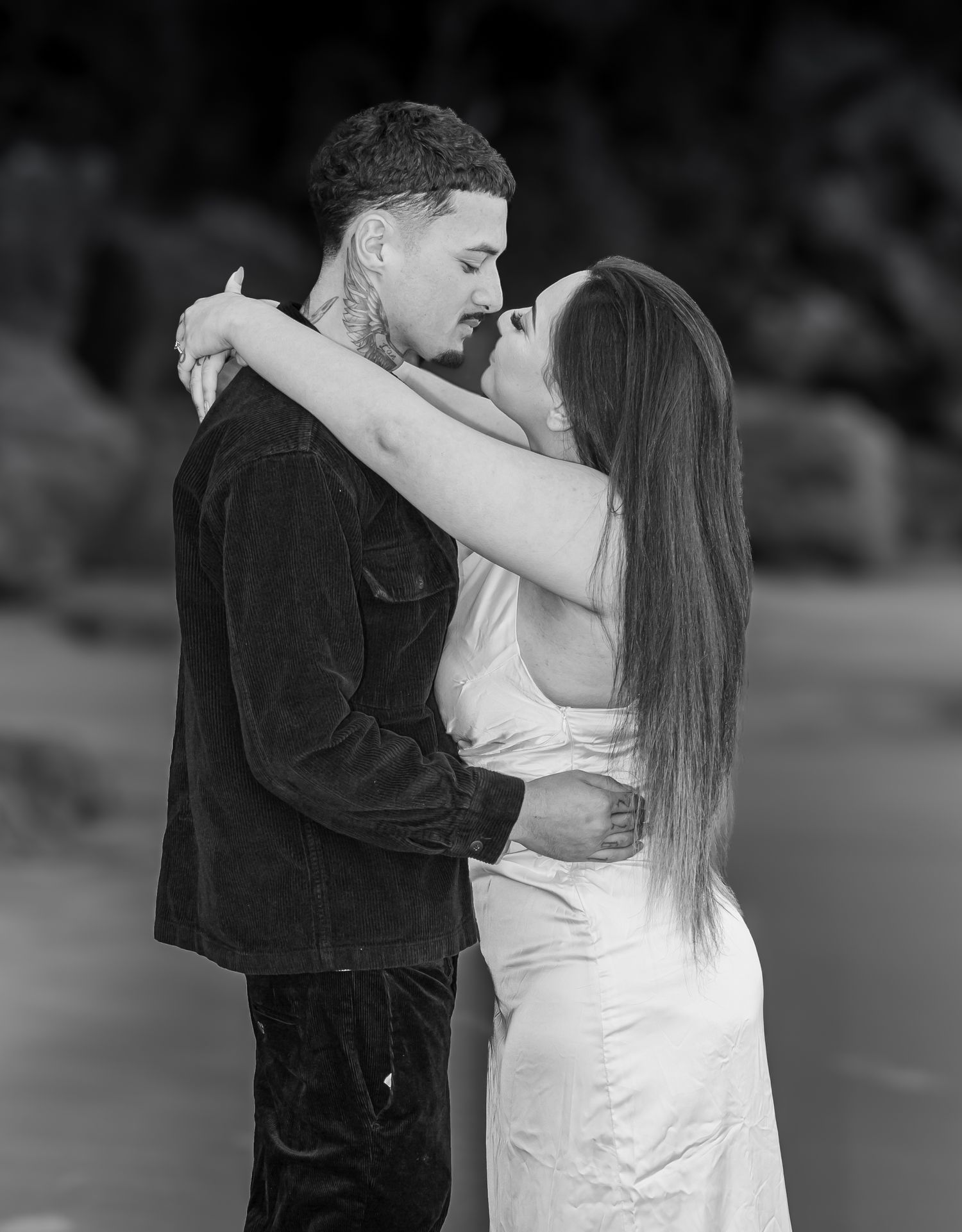 Couple sharing romantic kiss in black and white engagement photo on beach at sunset.