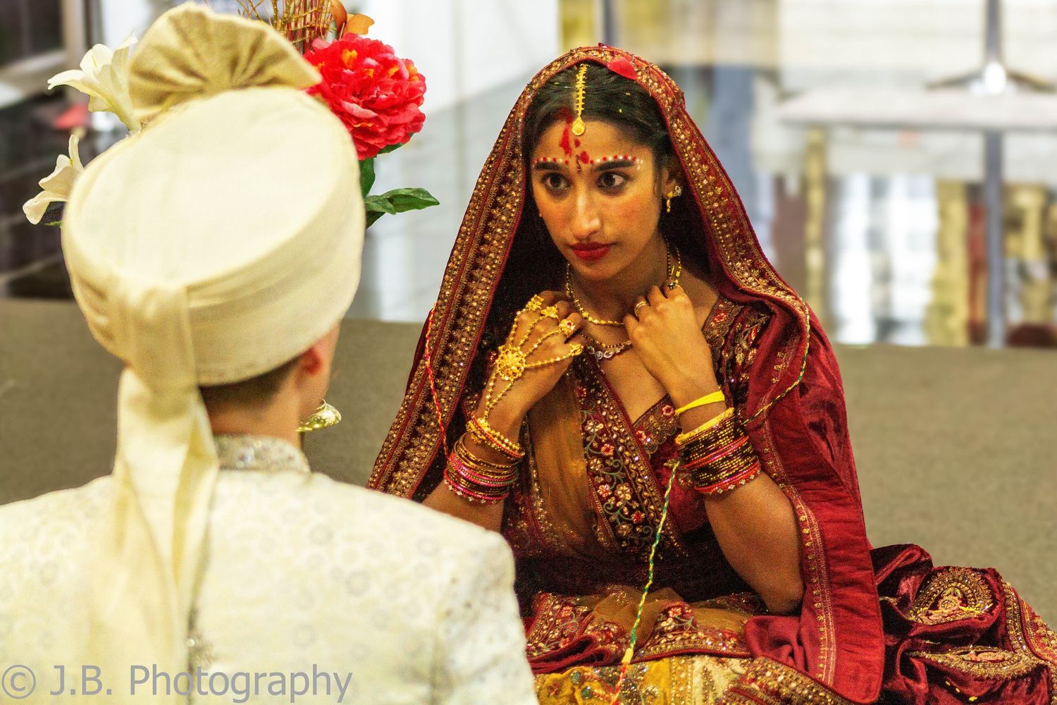 Indian bride in red and gold bridal attire with traditional jewelry during Hindu wedding ceremony.