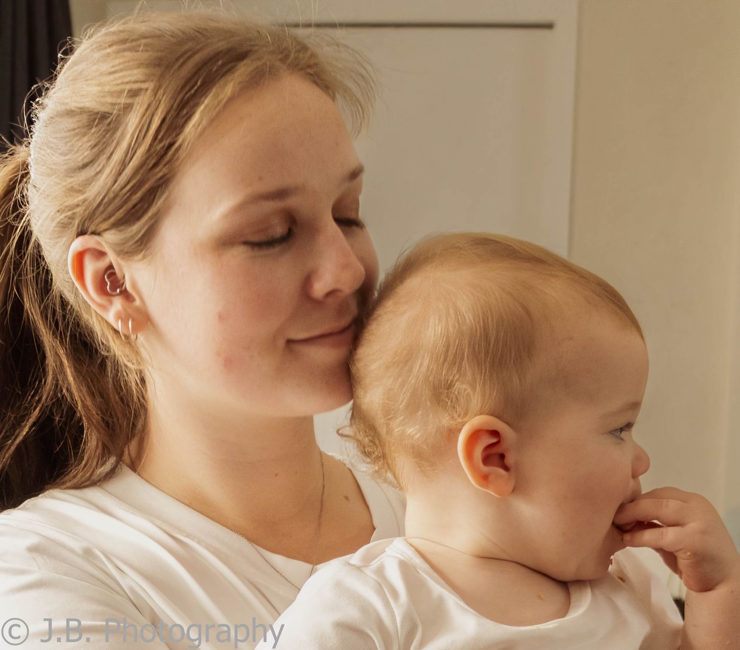 Young mother gently kisses her baby's head in a soft indoor portrait.