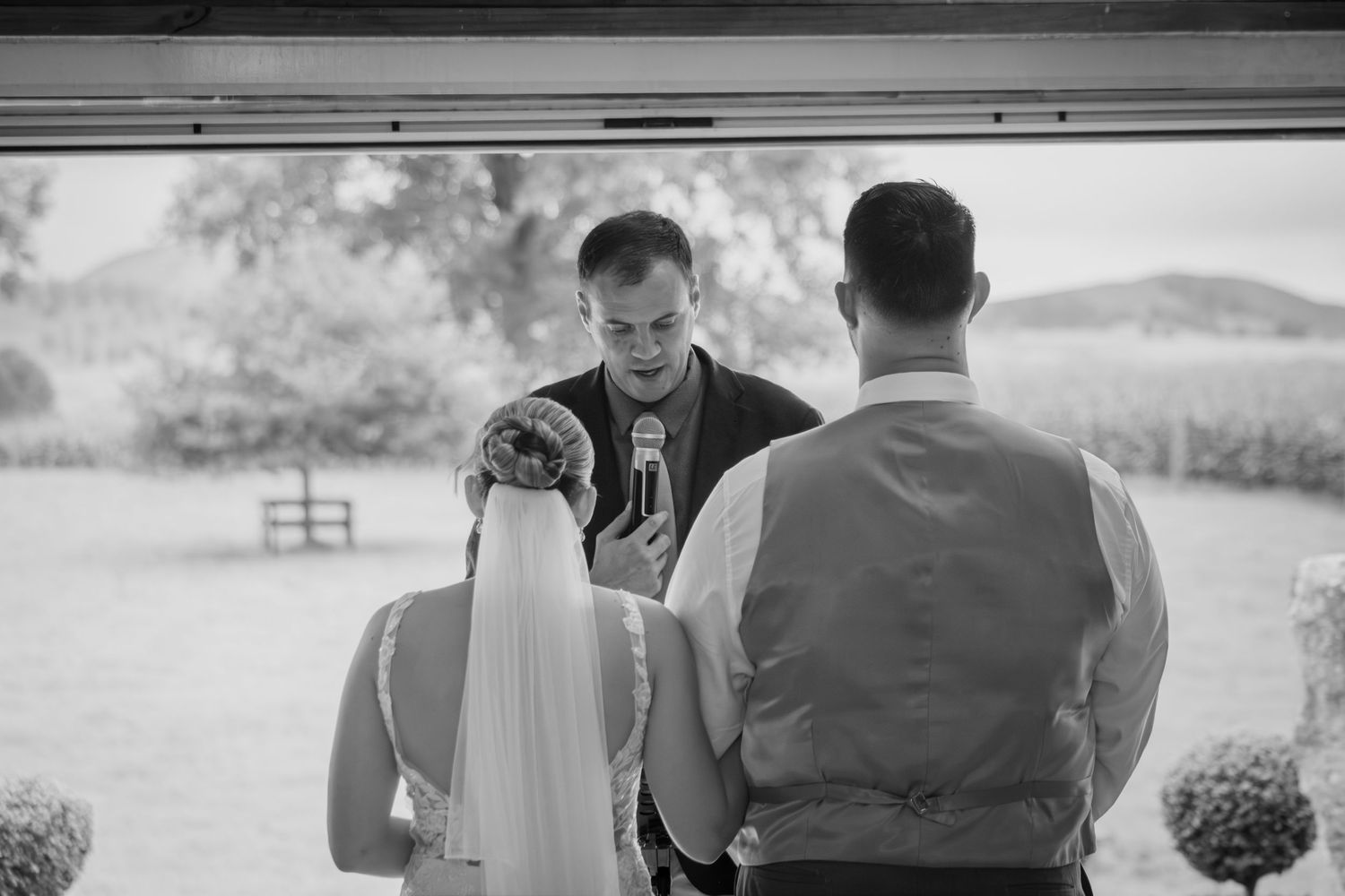 Officiant reads vows as bride and groom hold hands during outdoor wedding ceremony.