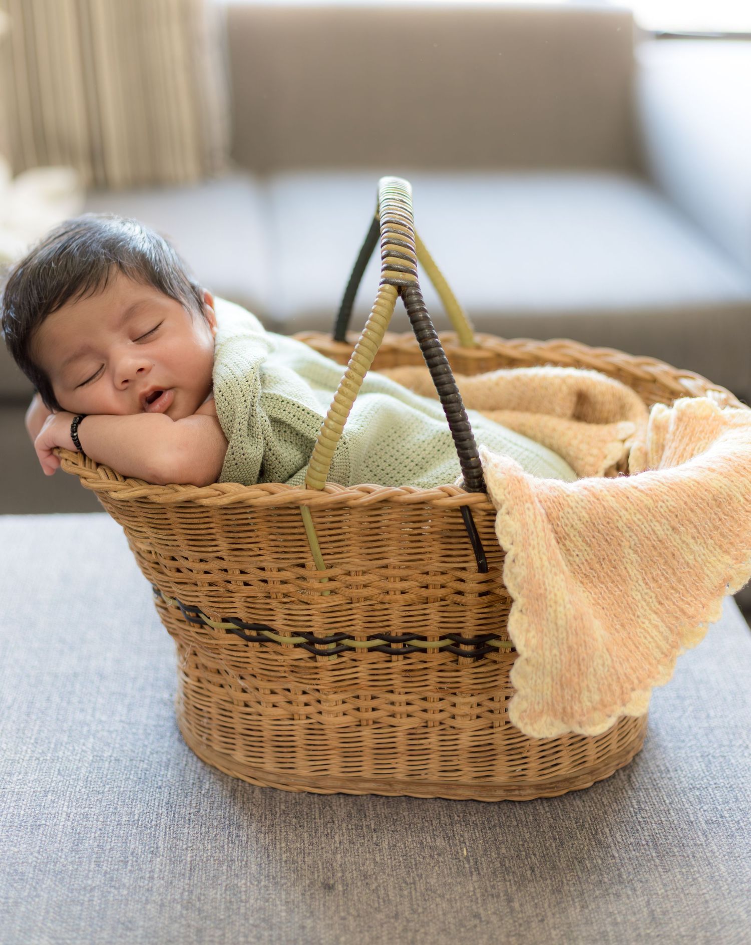Peacefully sleeping newborn baby in a green outfit inside a wicker basket with a blanket.