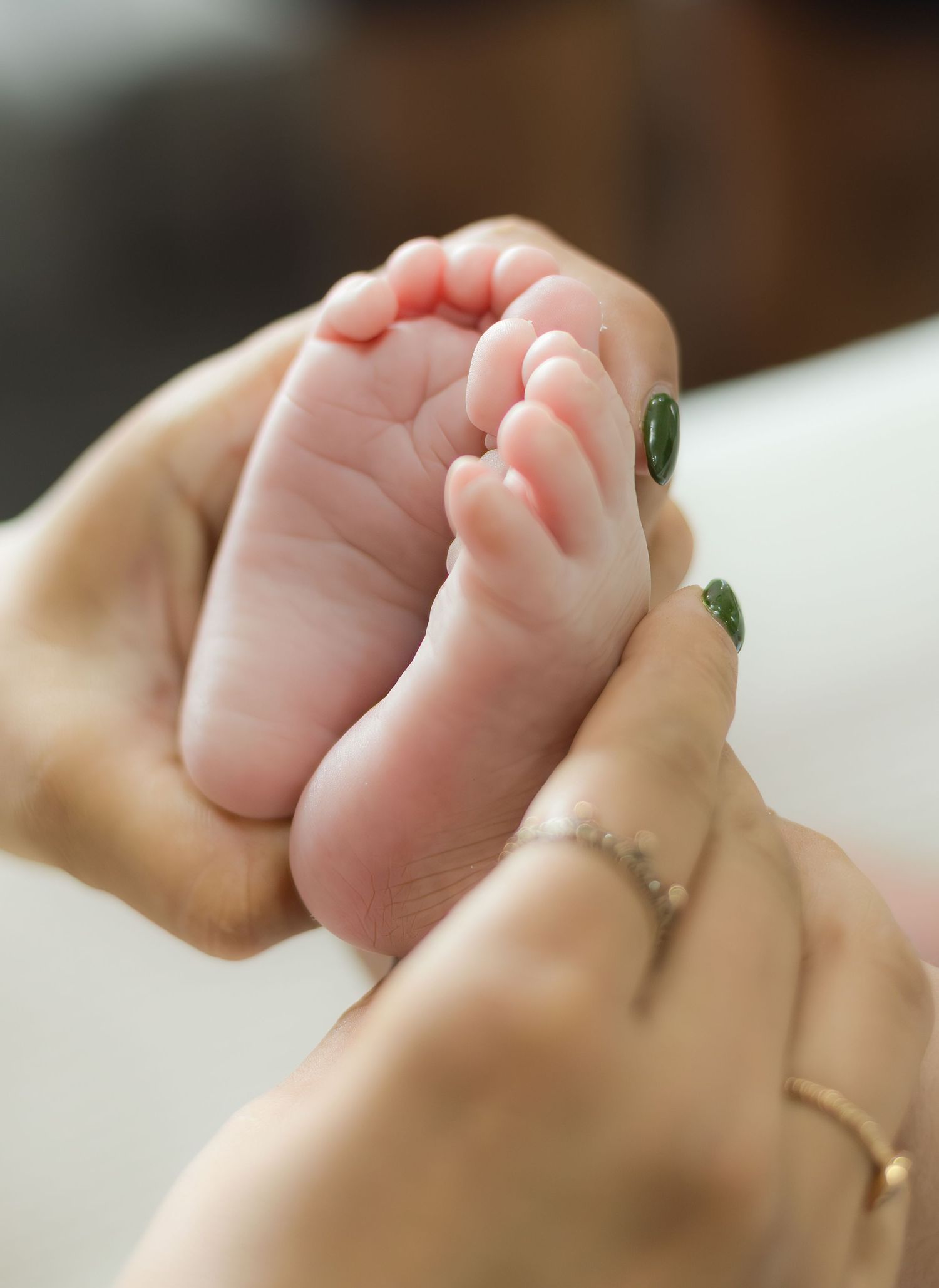 Close-up of a parent gently holding a newborn babys tiny feet with green nail polish.