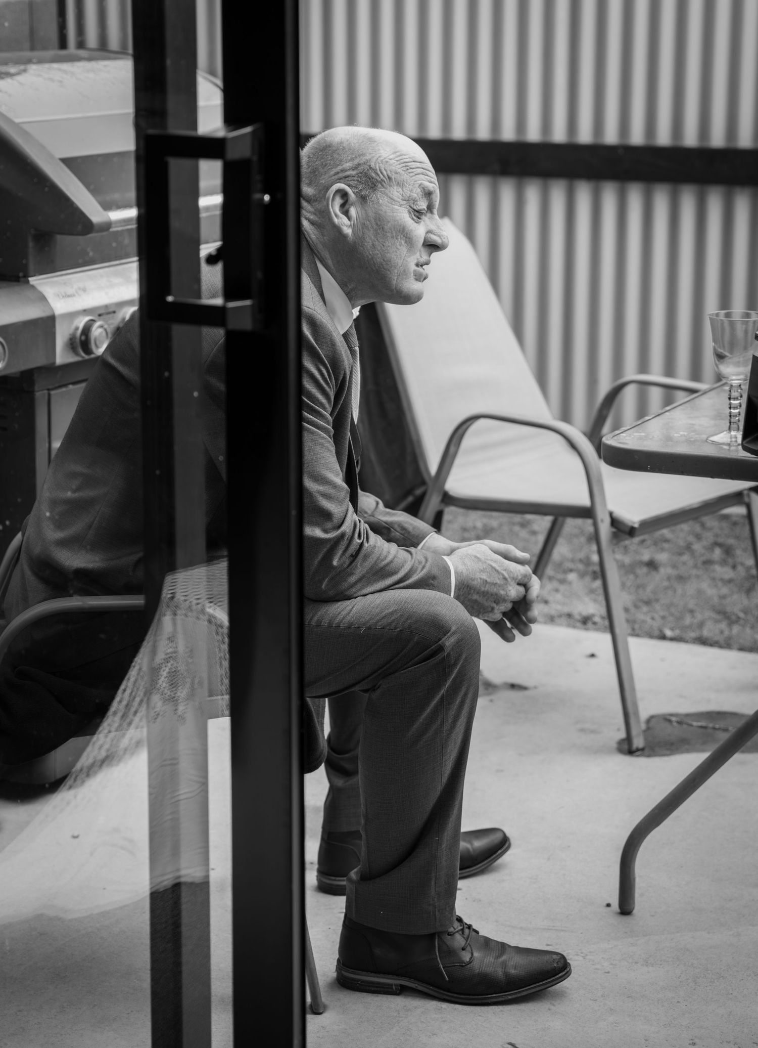 A bald man in a suit sits pensively in a chair in this black and white portrait photo.