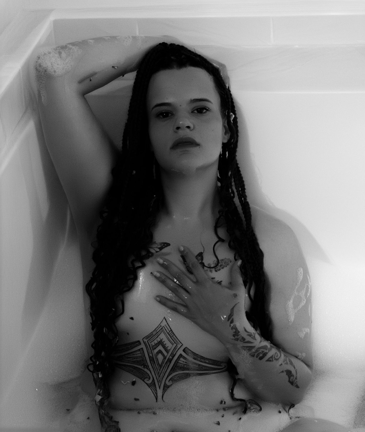 Black and white artistic portrait of tattooed woman with long hair posing in a bathtub.
