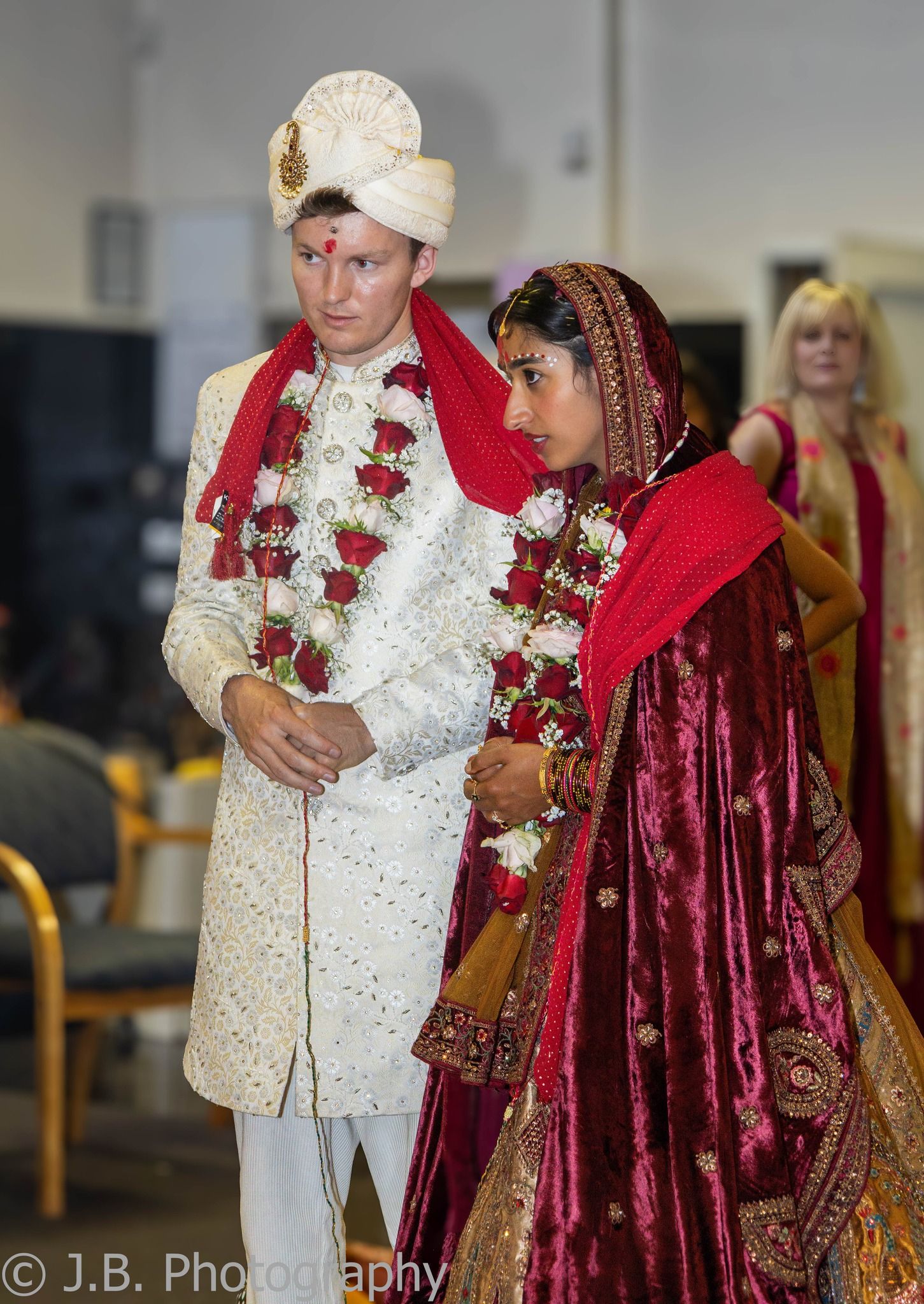 Groom in white sherwani and bride in red lehenga walk together during traditional Hindu wedding.