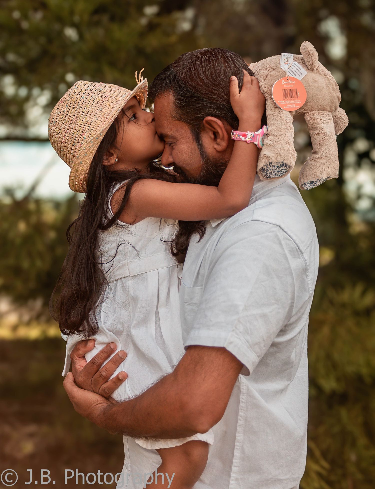 Father shares a sweet nose kiss with his young daughter holding a stuffed animal.