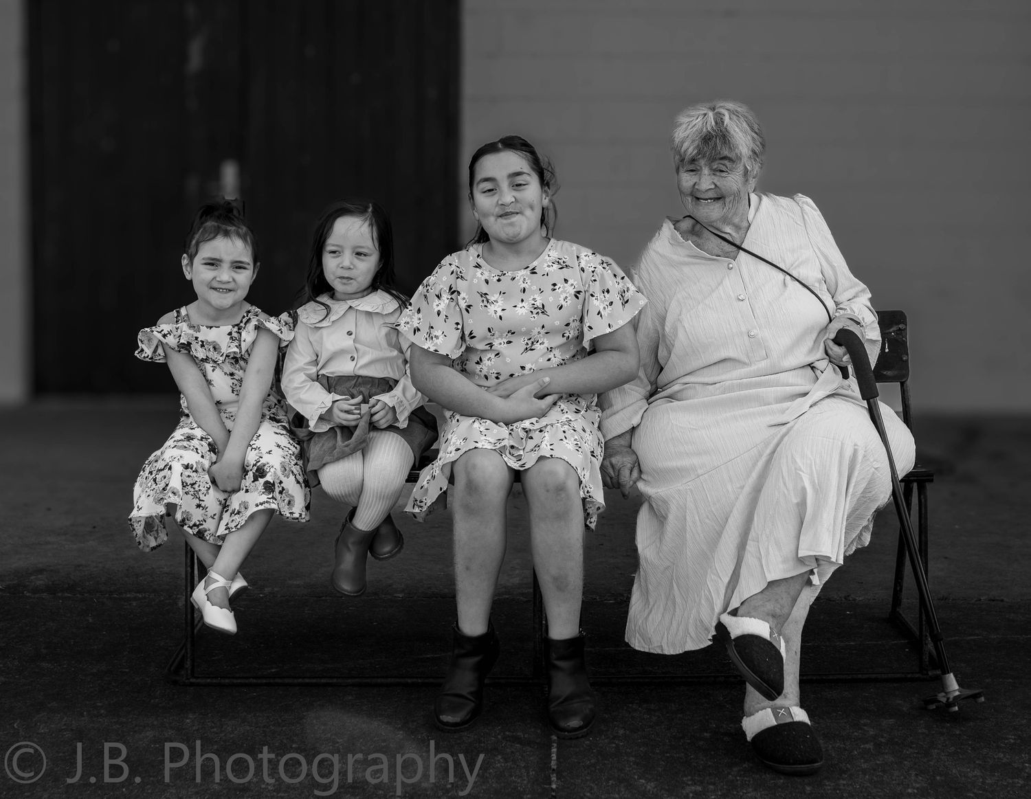Grandmother sits on a bench with three young girls in matching dresses in black and white.