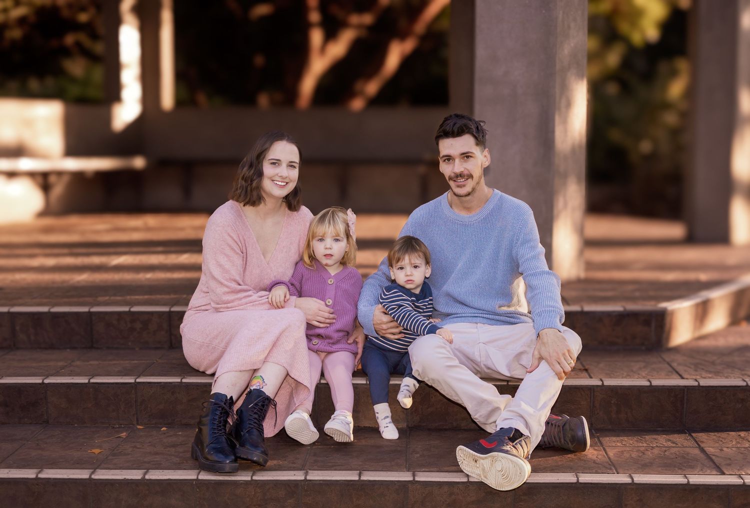 Young family with two toddlers sitting on brick steps outdoors for a casual portrait session.