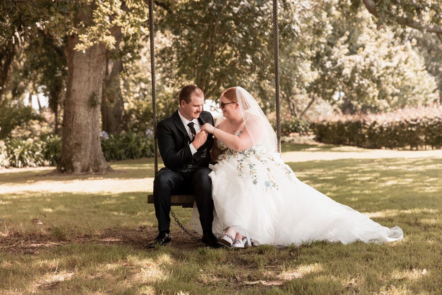 Bride and groom sit together on garden swing sharing a tender moment outdoors.