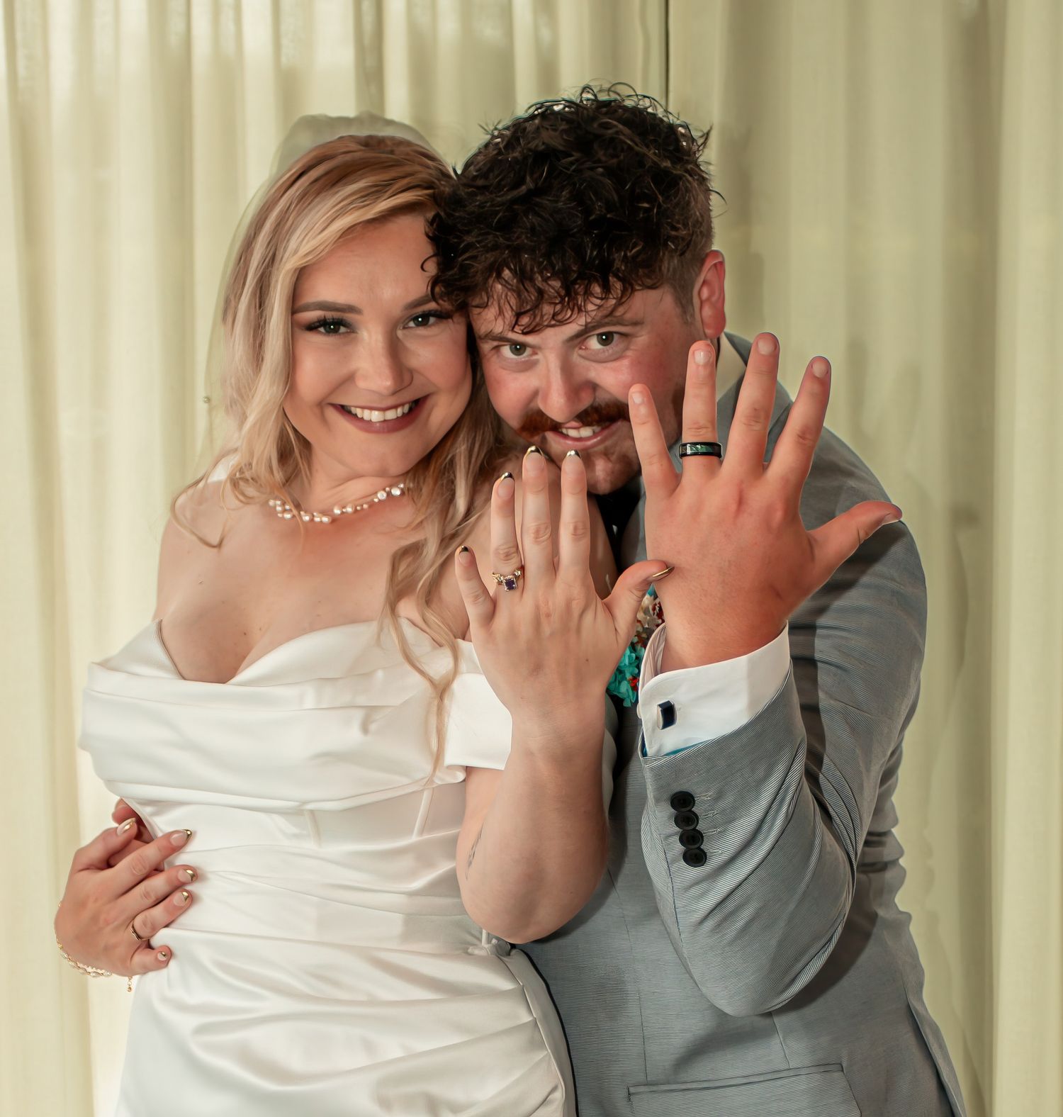Newlyweds smiling and showing off their wedding rings in a joyful wedding portrait.