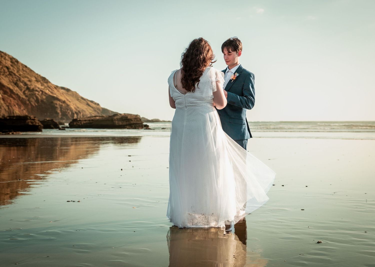 Bride and groom dancing on reflective beach at golden sunset in romantic wedding photo.