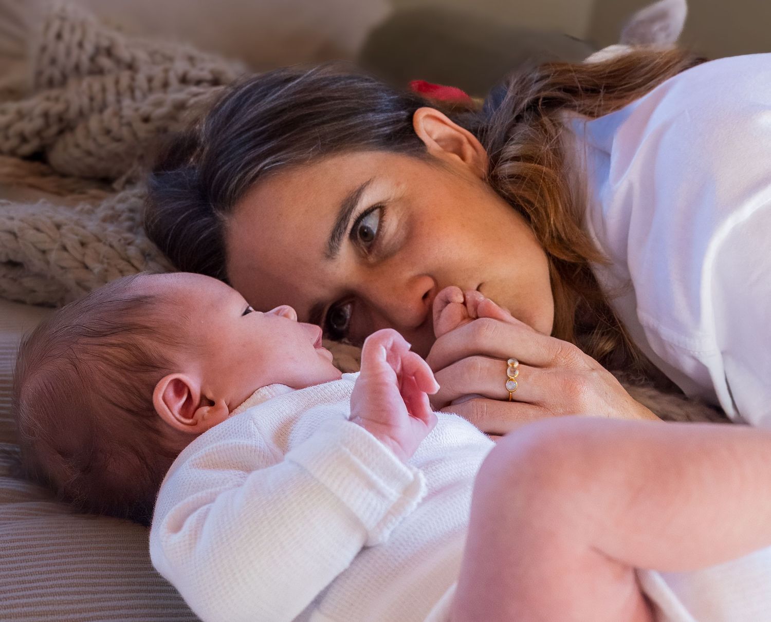 Mother lying beside newborn baby on a bed, gazing softly at her infant in an intimate portrait.