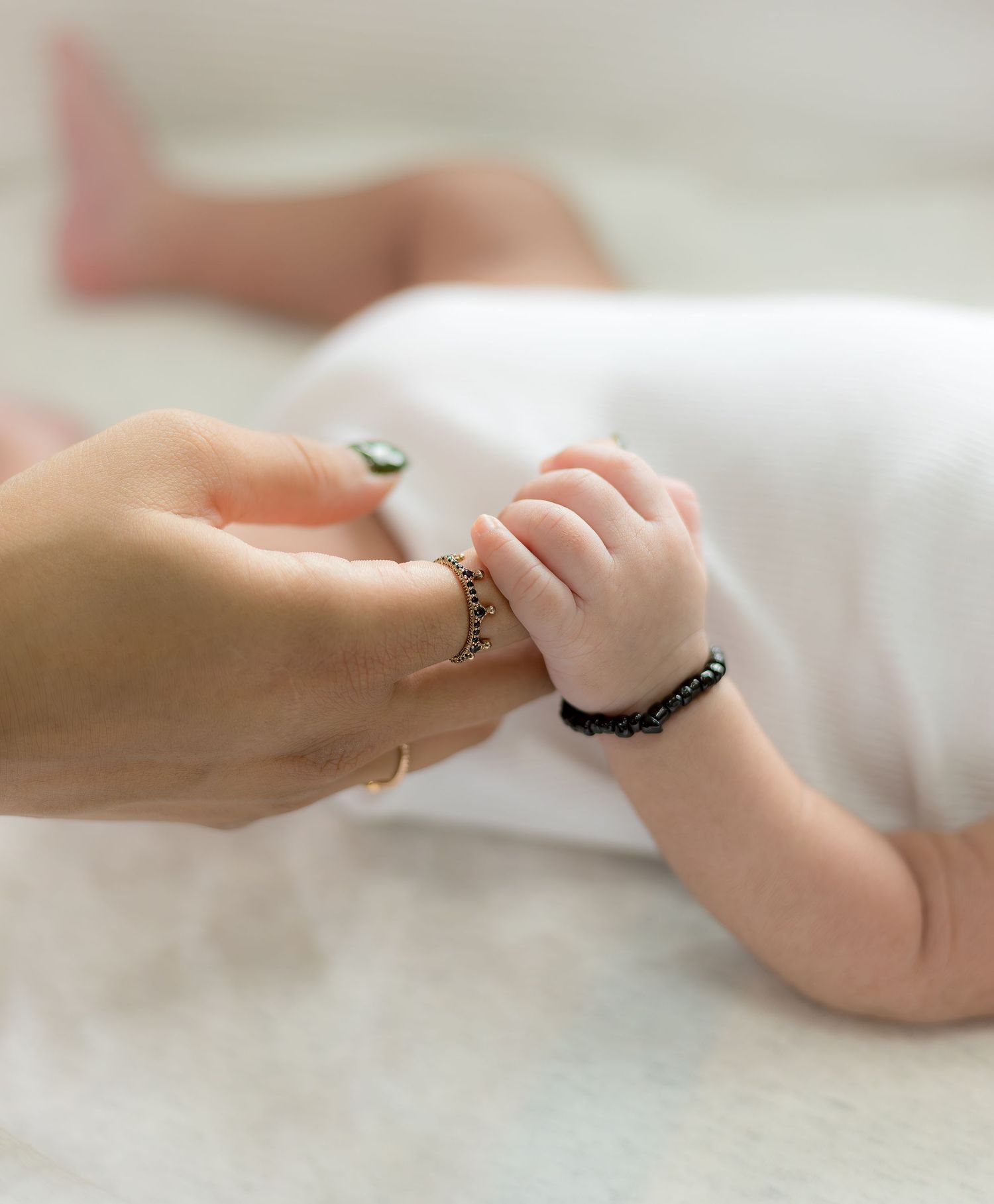 Newborn baby grasping a parents finger wearing rings and bracelets on a white surface.