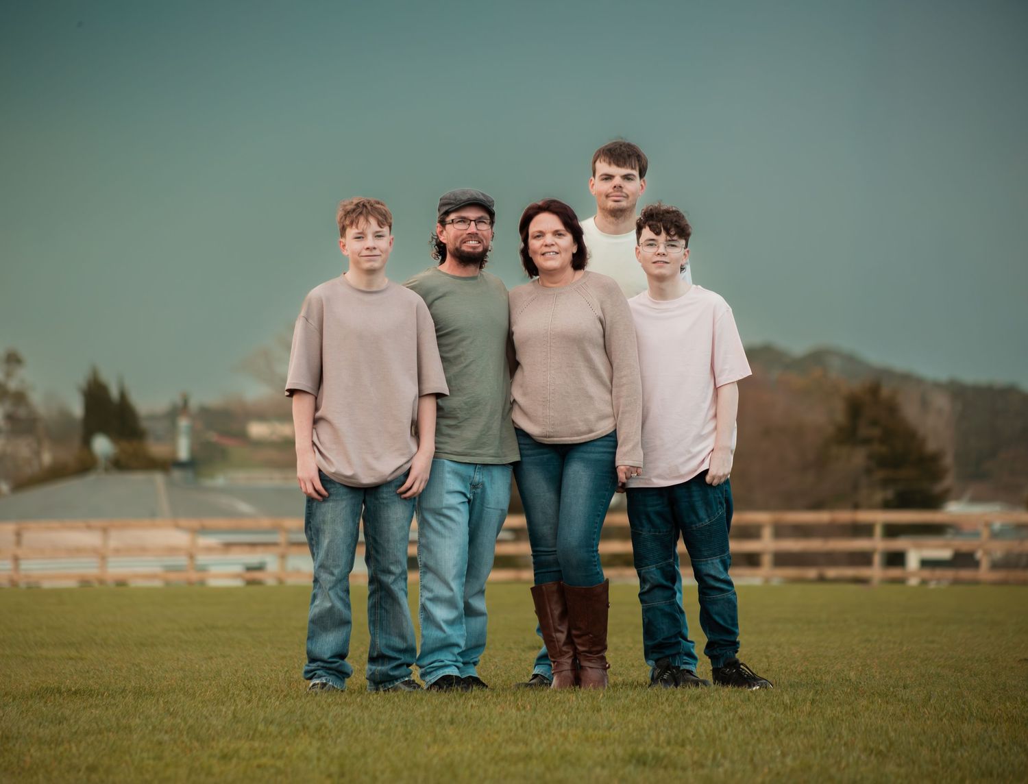 Family of five standing together in an open green field under a dramatic sky.
