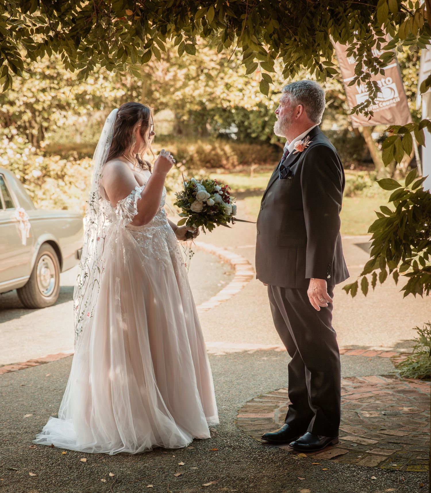 Emotional bride in lace gown sharing first look moment with father under autumn trees.