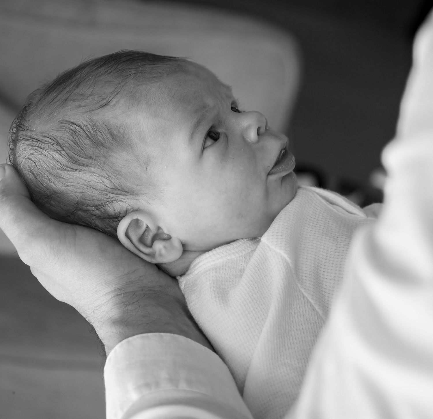 Black and white close-up portrait of a newborn baby being cradled in an adult's supportive hands.