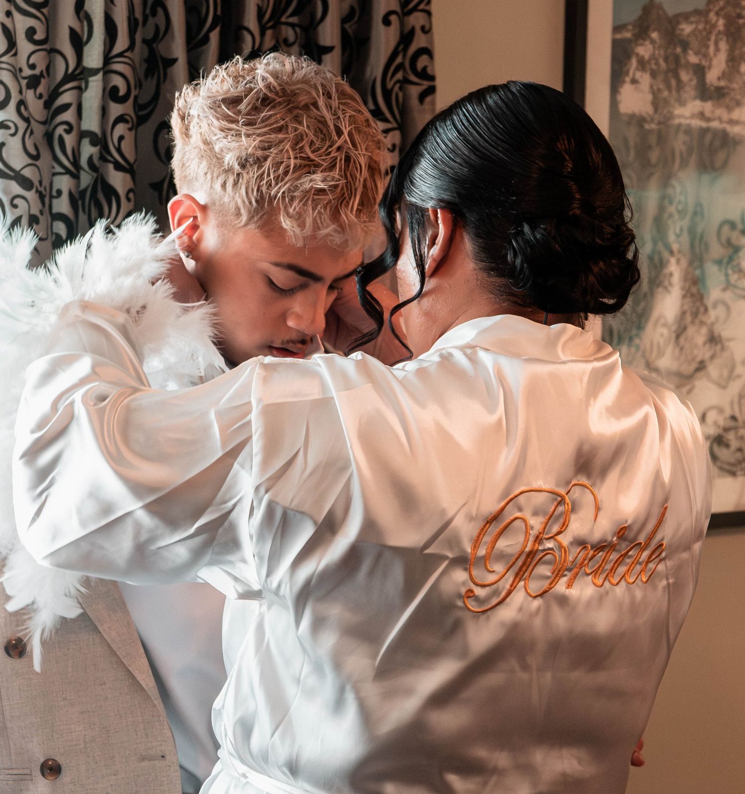 Couple in white satin robes embrace tenderly, bride wearing embroidered Bride robe on wedding day.